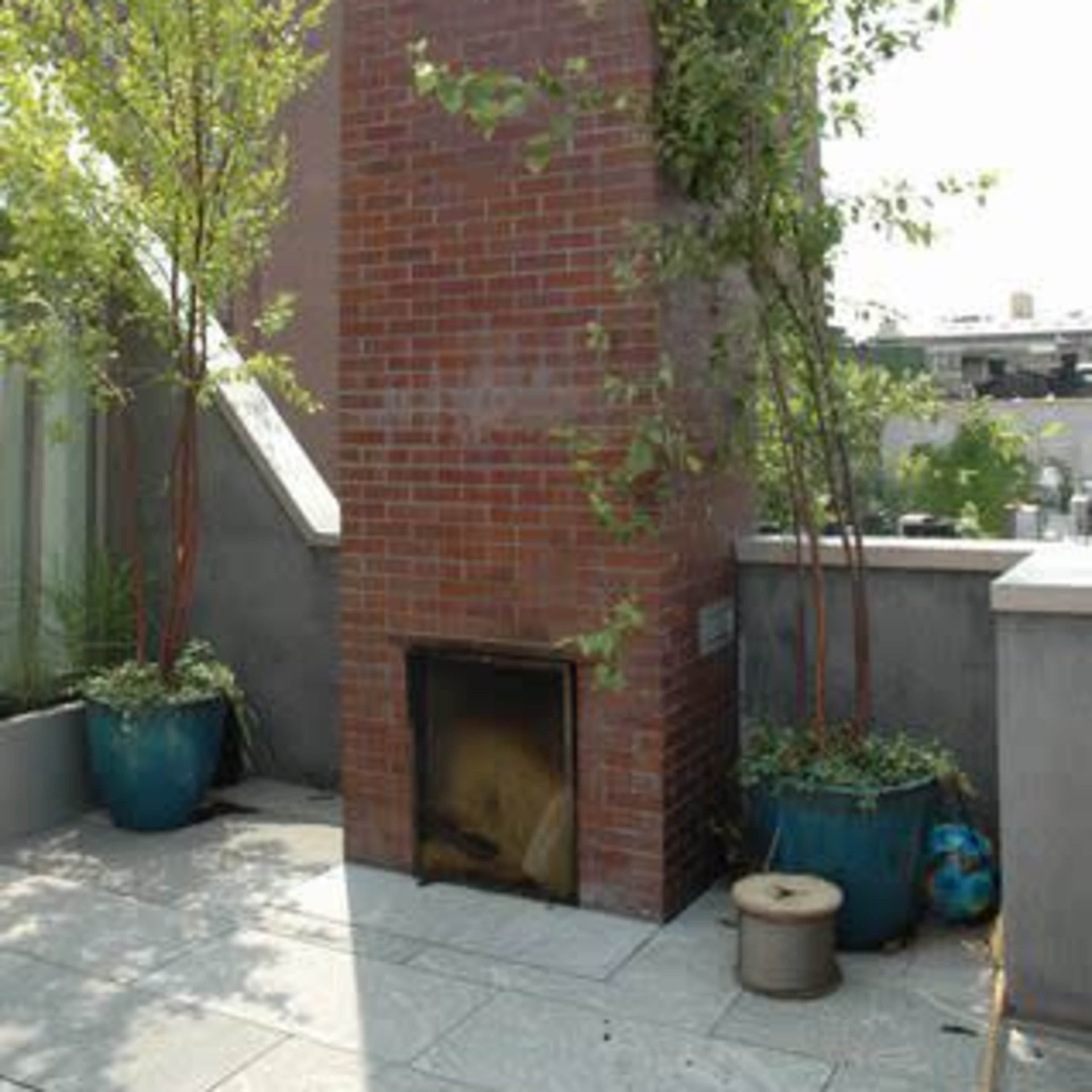 A brick outdoor chimney structure is surrounded by potted plants on a rooftop terrace.