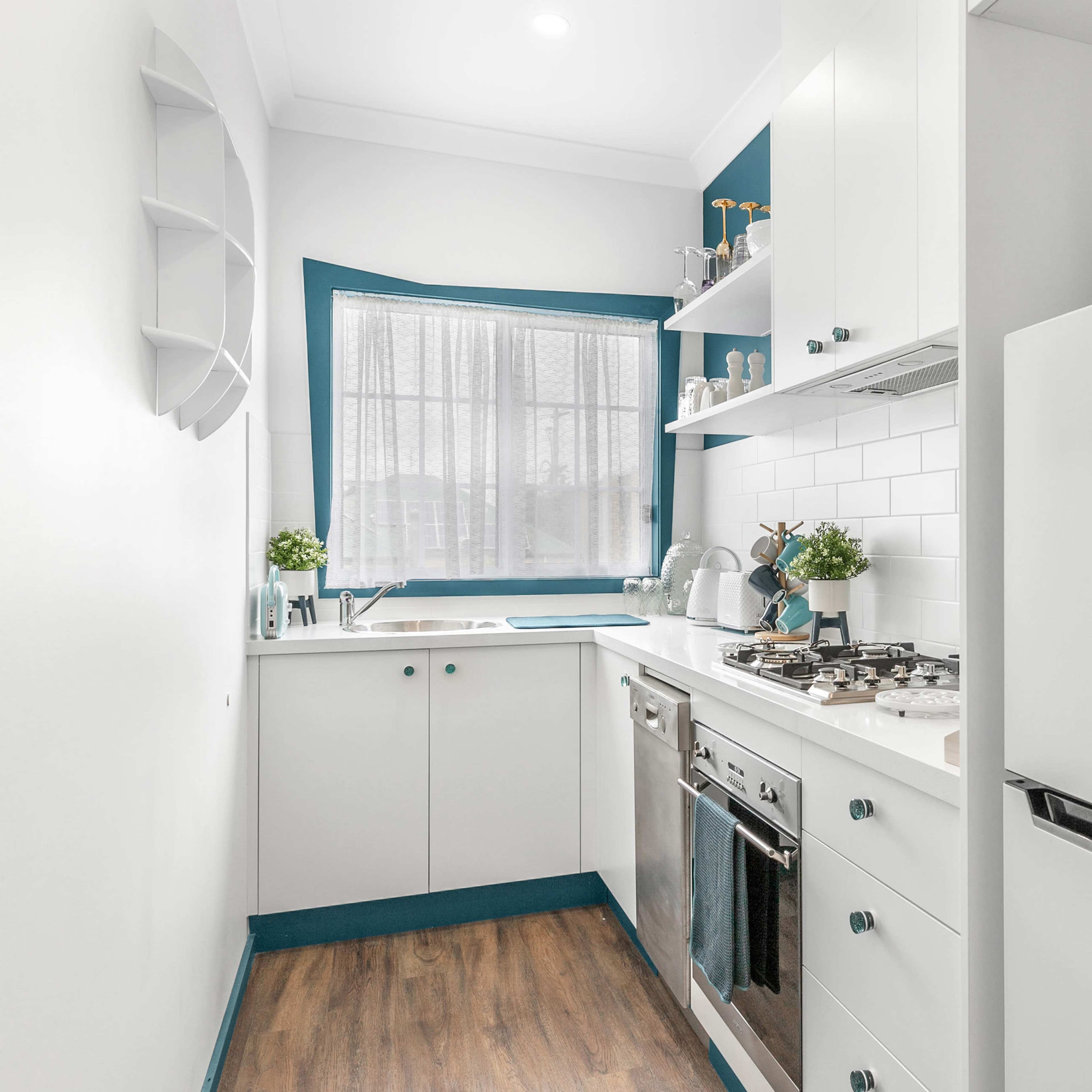 A compact kitchen featuring white cabinets, a stainless steel stove, a refrigerator, and a window with a view.