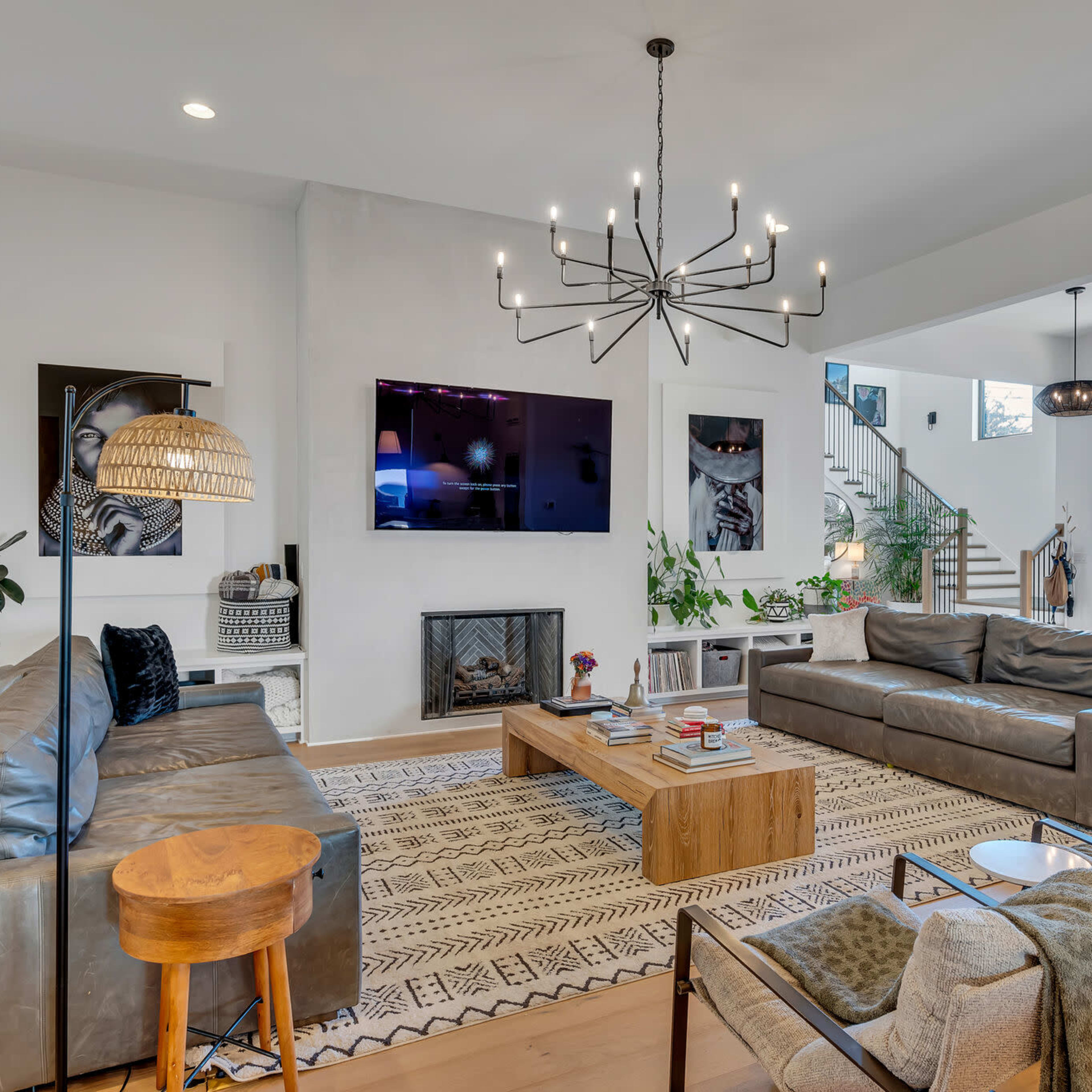 A modern living room features two leather sofas facing a wooden coffee table, a television mounted on the wall, and a staircase in the background.