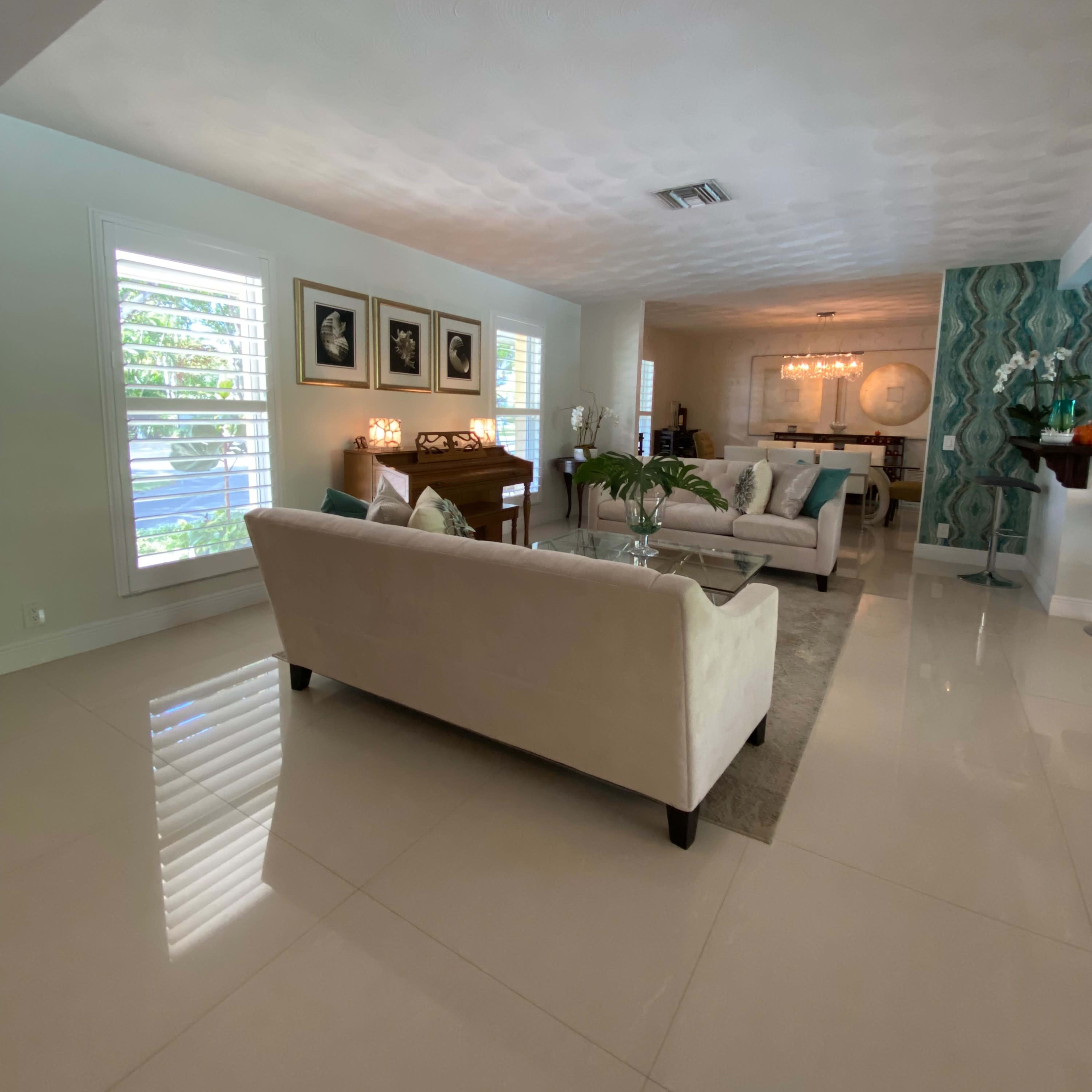 A modern living room with white furniture, polished tile floors, and large windows allowing natural light to enter.