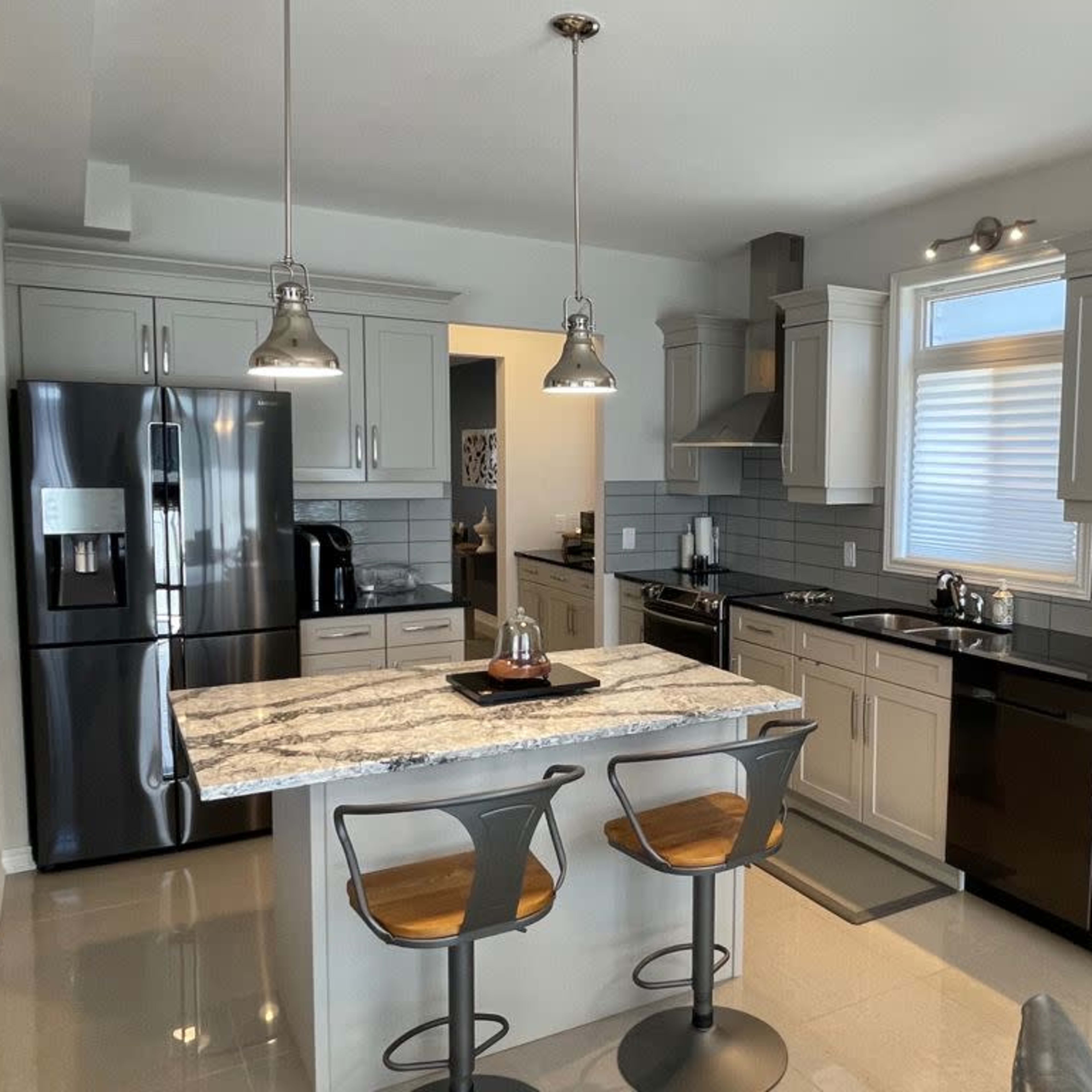 A modern kitchen featuring light gray cabinets, a large island with two bar stools, stainless steel appliances, and a black countertop.