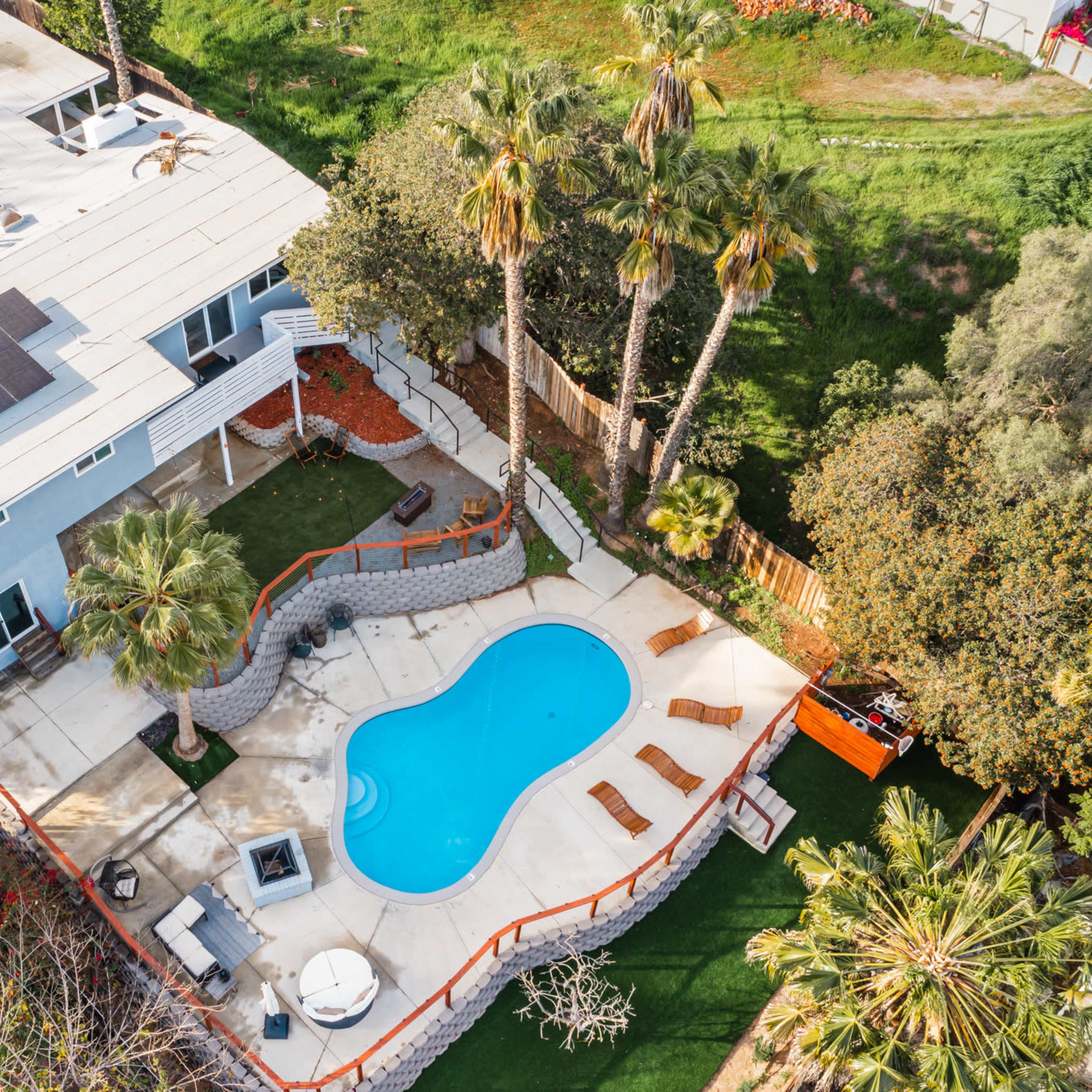An aerial view of a residential property featuring a swimming pool surrounded by palm trees and an outdoor seating area.
