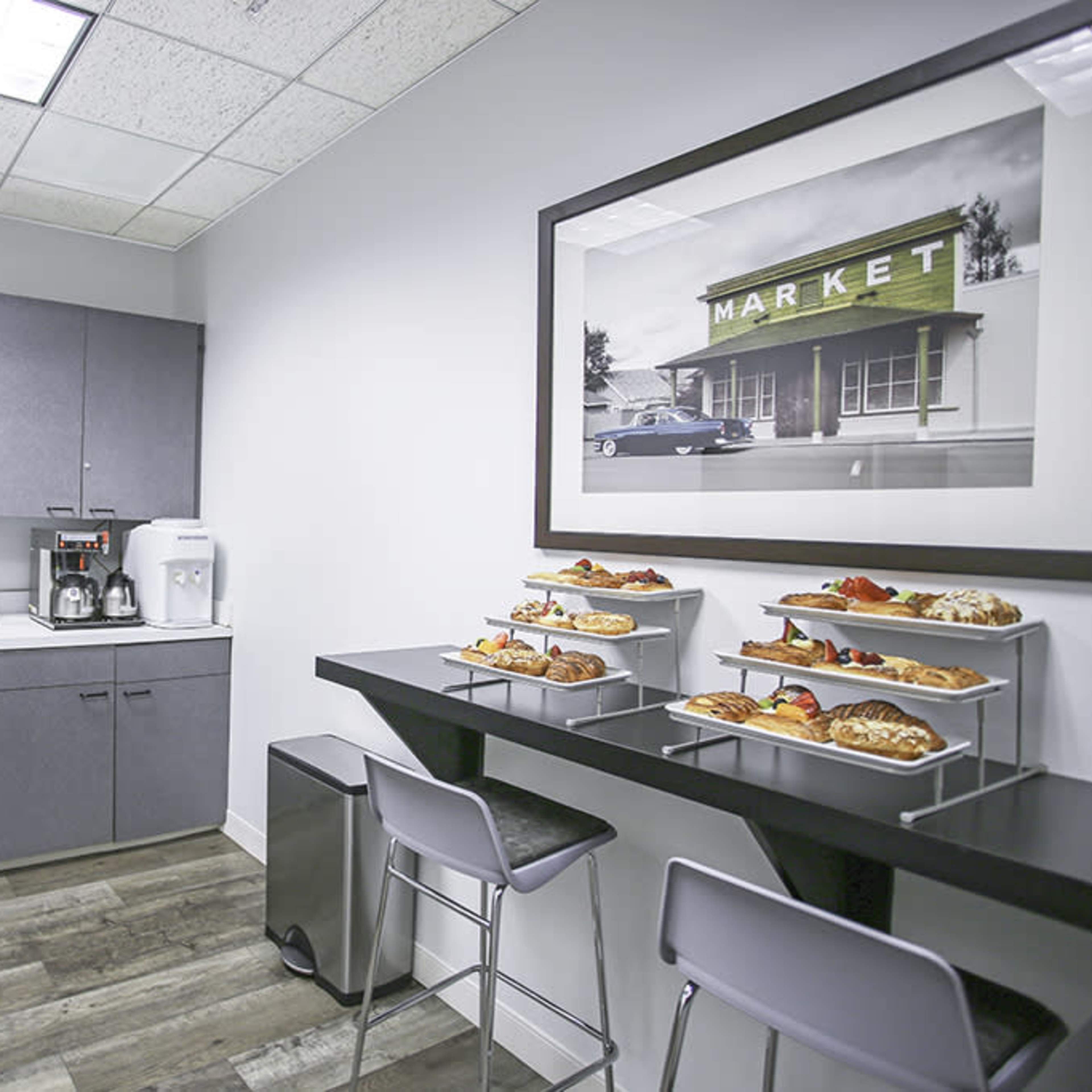 A modern kitchen area with gray cabinets, a stainless steel refrigerator, and a table displaying a variety of food items.