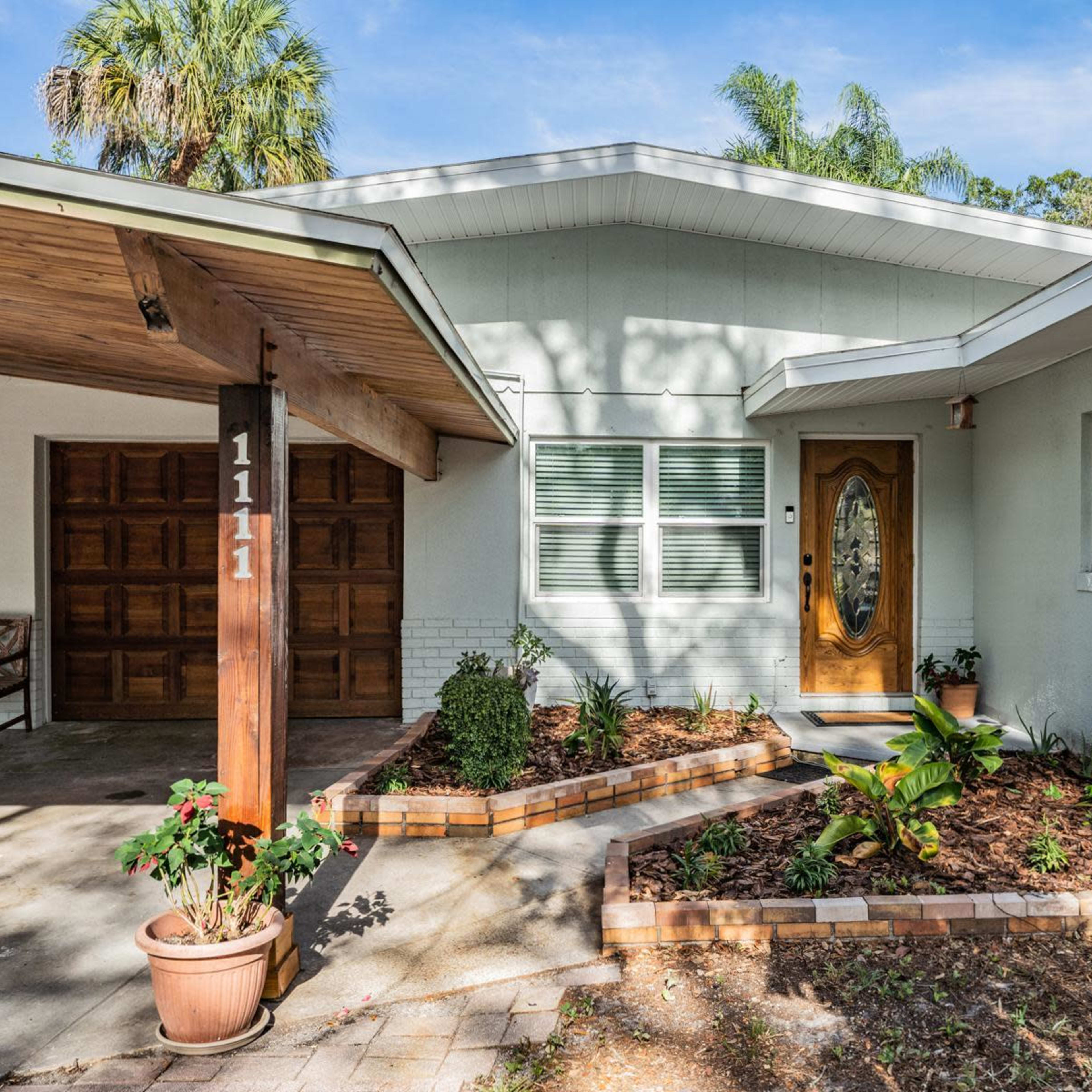 A residential house with a landscaped front yard, a covered carport, and a wooden door next to large windows.