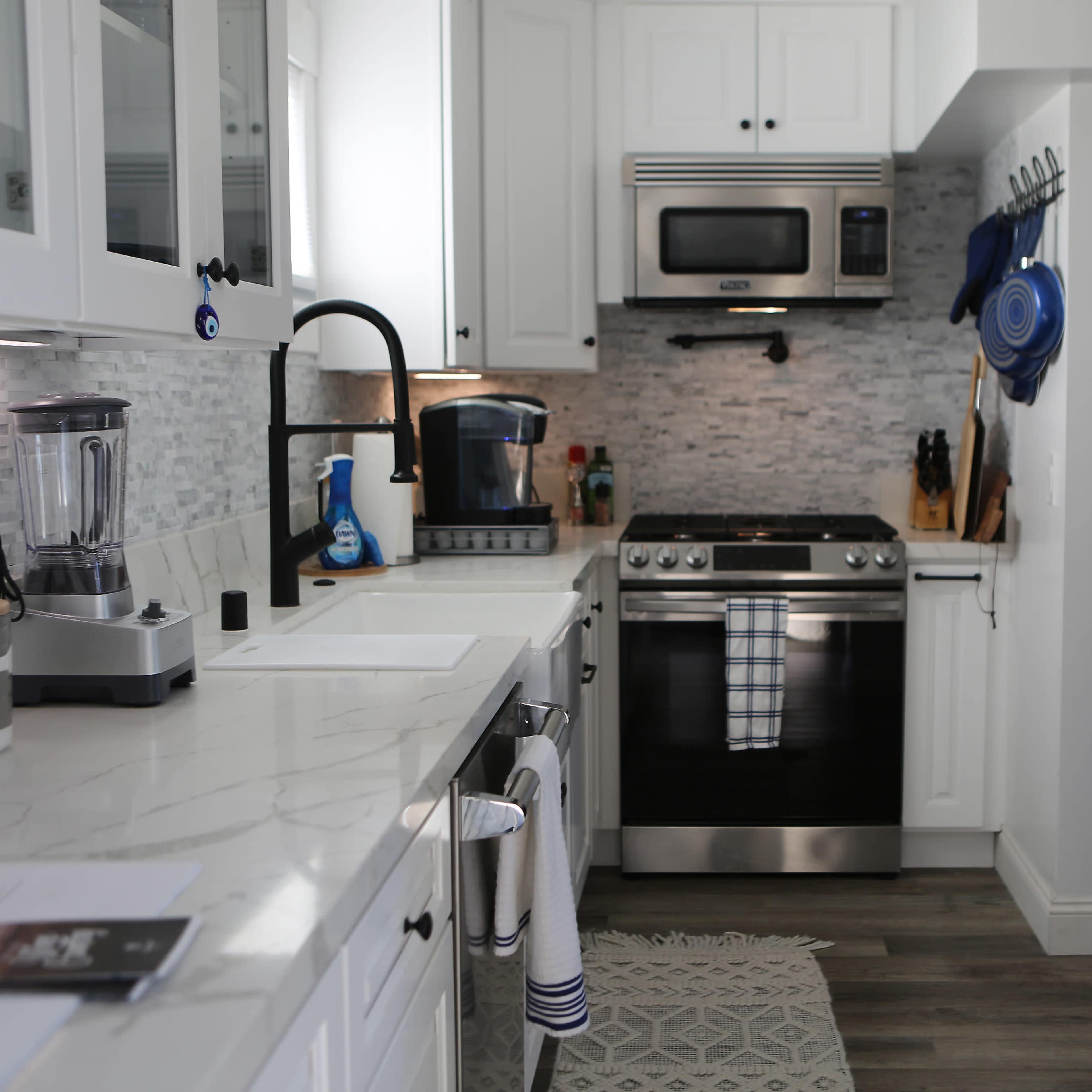 A modern kitchen with white cabinets, stainless steel appliances, and a marble countertop.