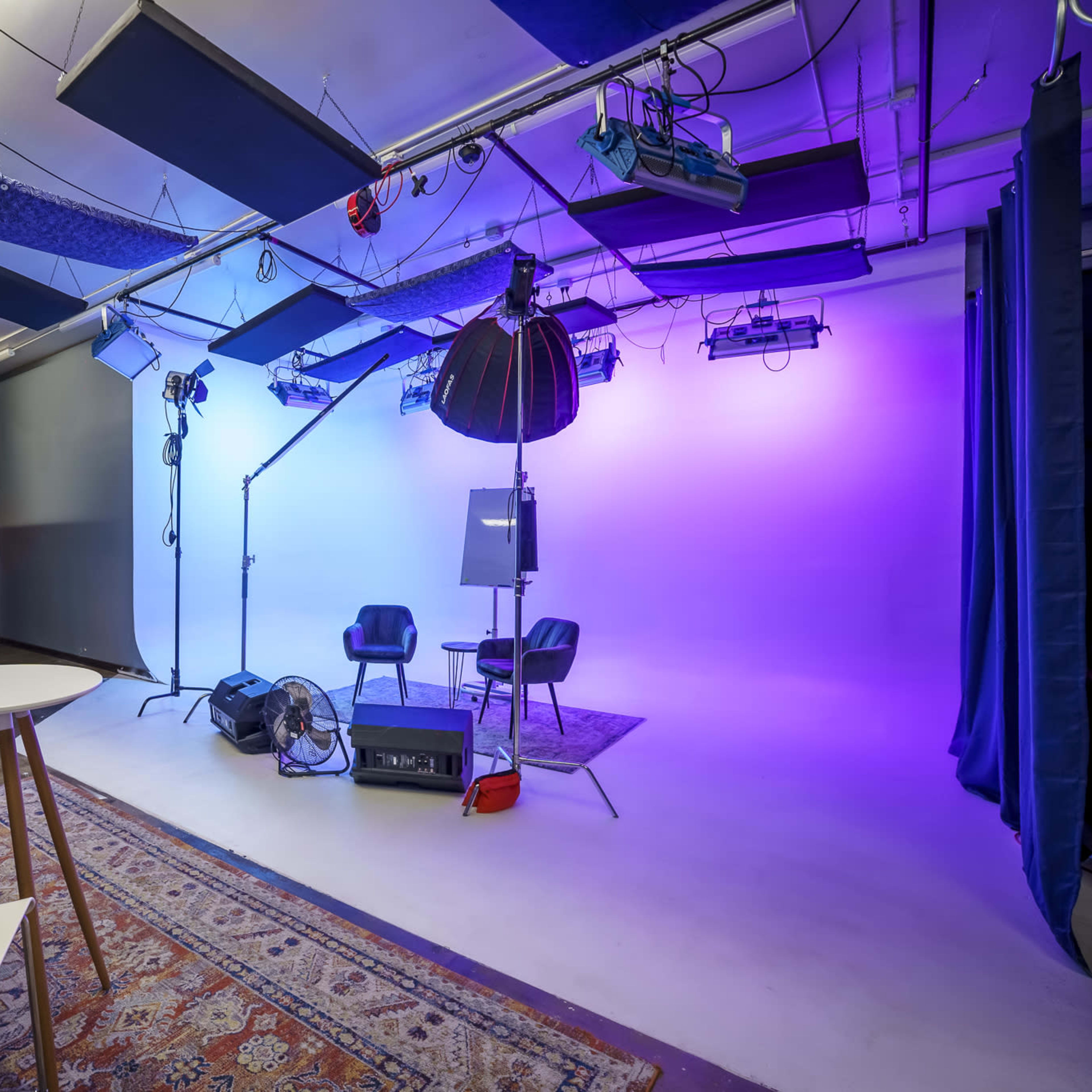 A photography studio is set up with lights, chairs, and a backdrop illuminated in purple and blue.