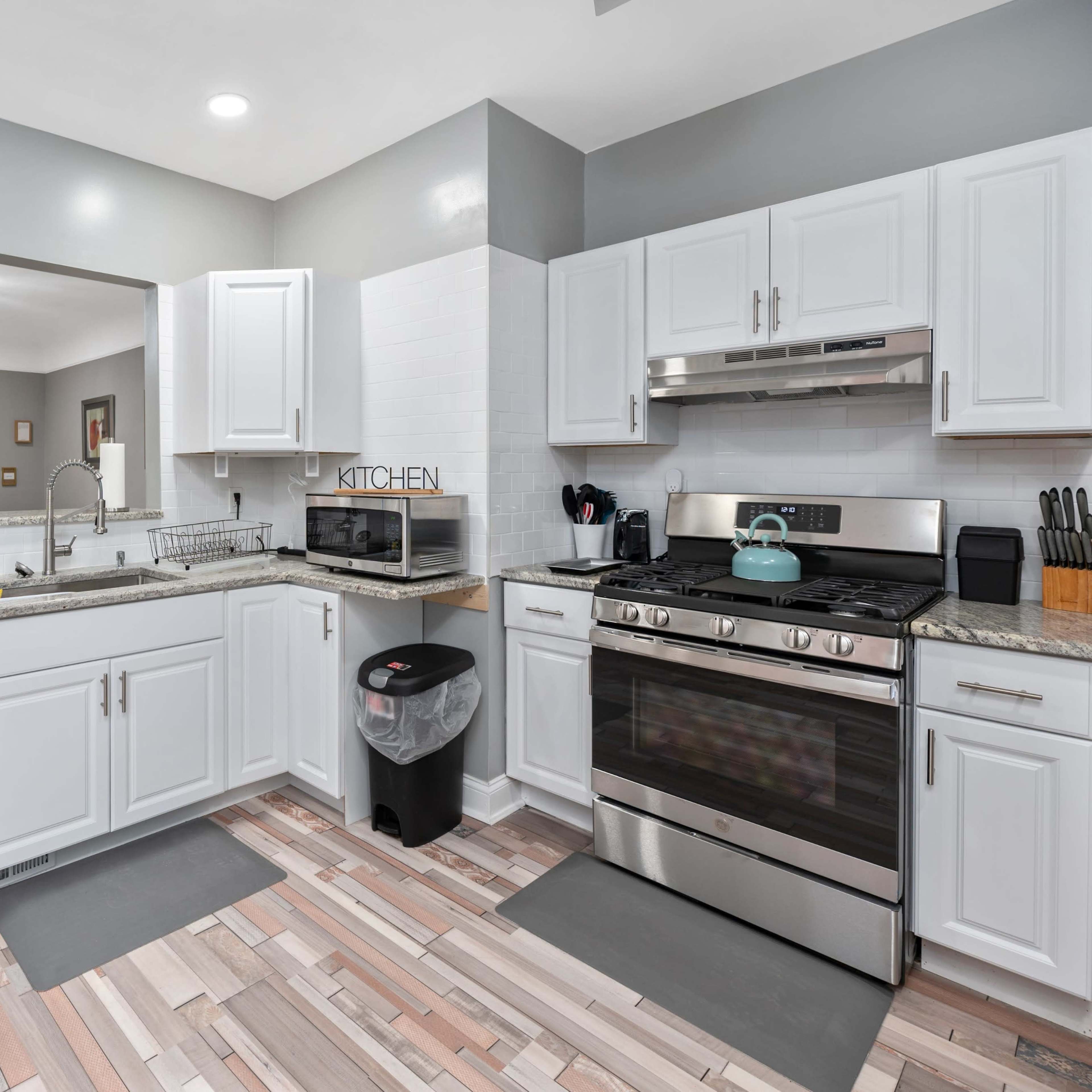 A modern kitchen with white cabinetry, stainless steel appliances, and a granite countertop, overlooking a living area through an open layout.