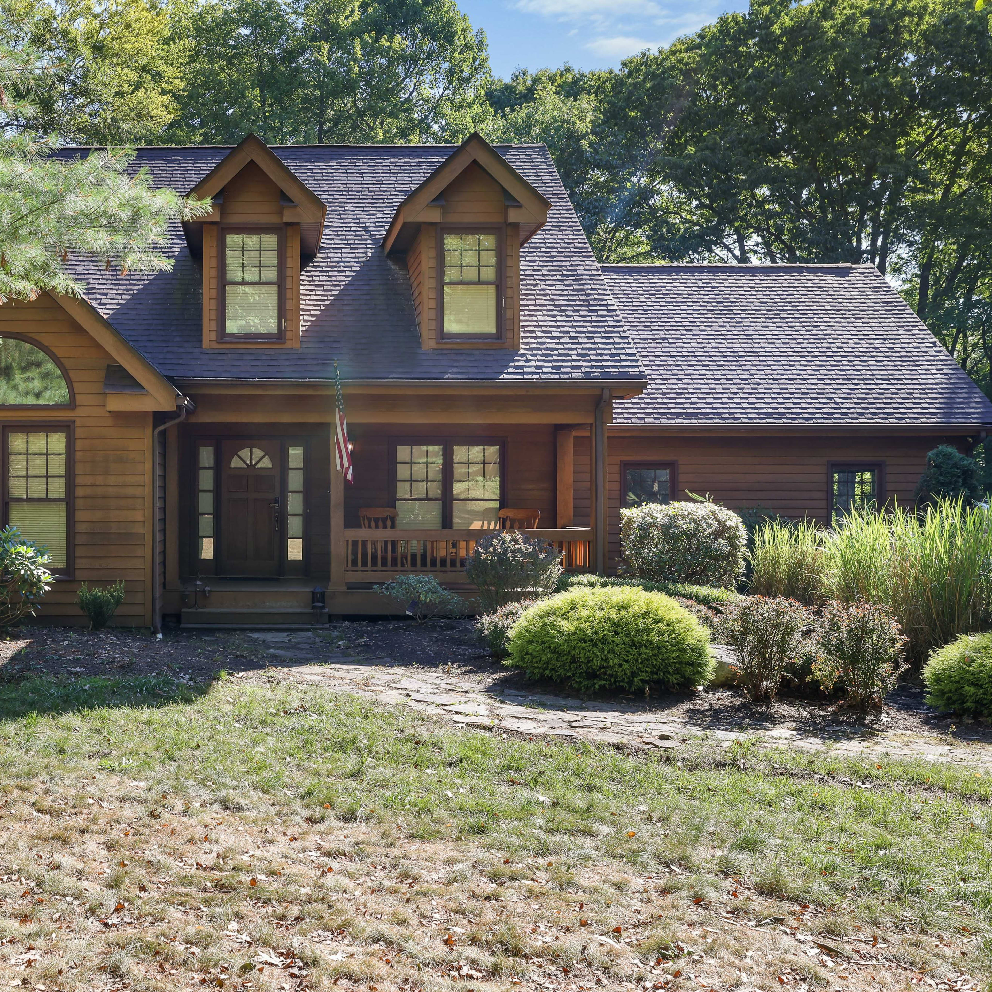 A large wooden house surrounded by green trees and shrubs, with a pathway leading to the front door.
