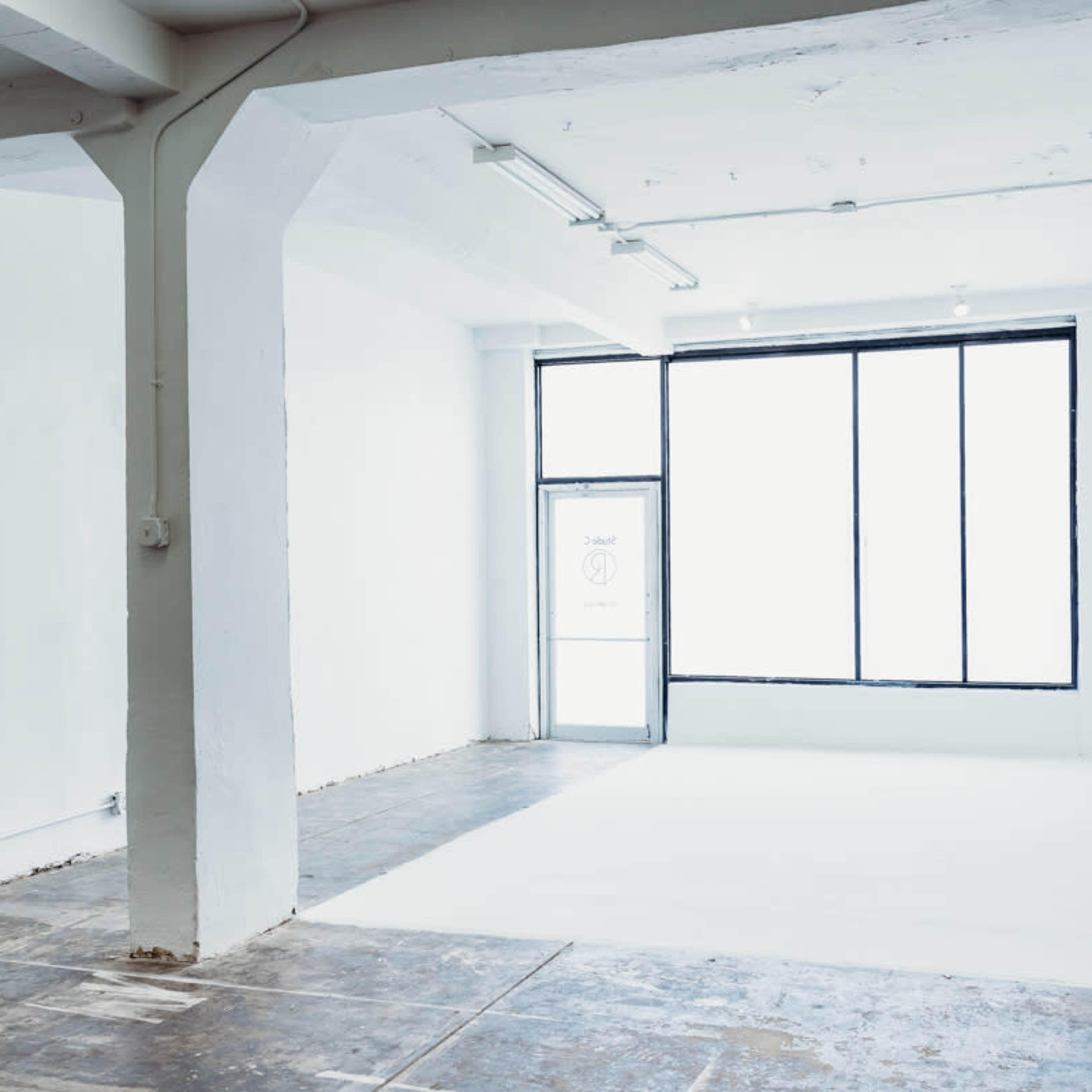 A minimalist, empty interior space with white walls, a large window, and a door.