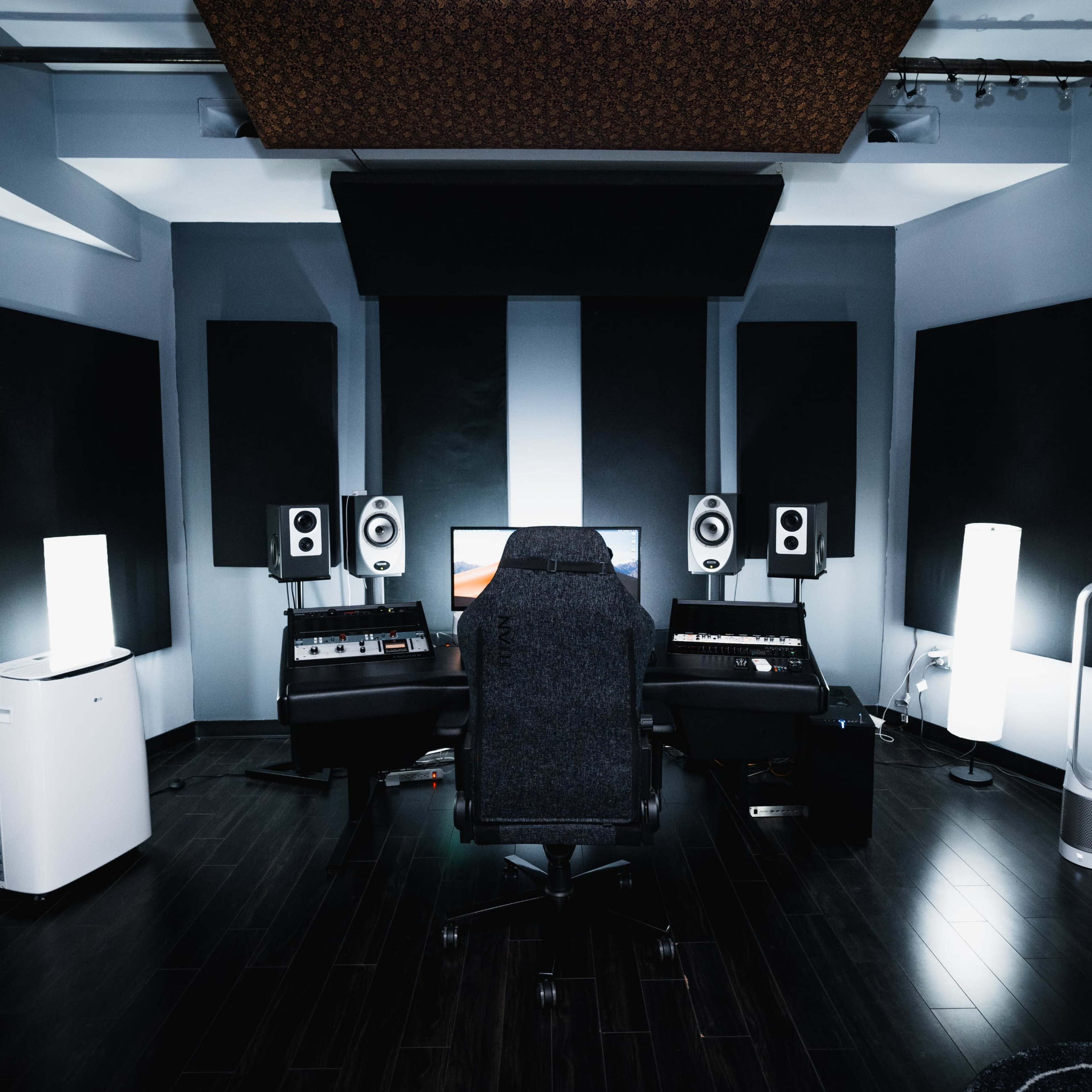 A well-equipped music studio with a central black chair, surrounded by soundproof panels, speakers, and various audio equipment.