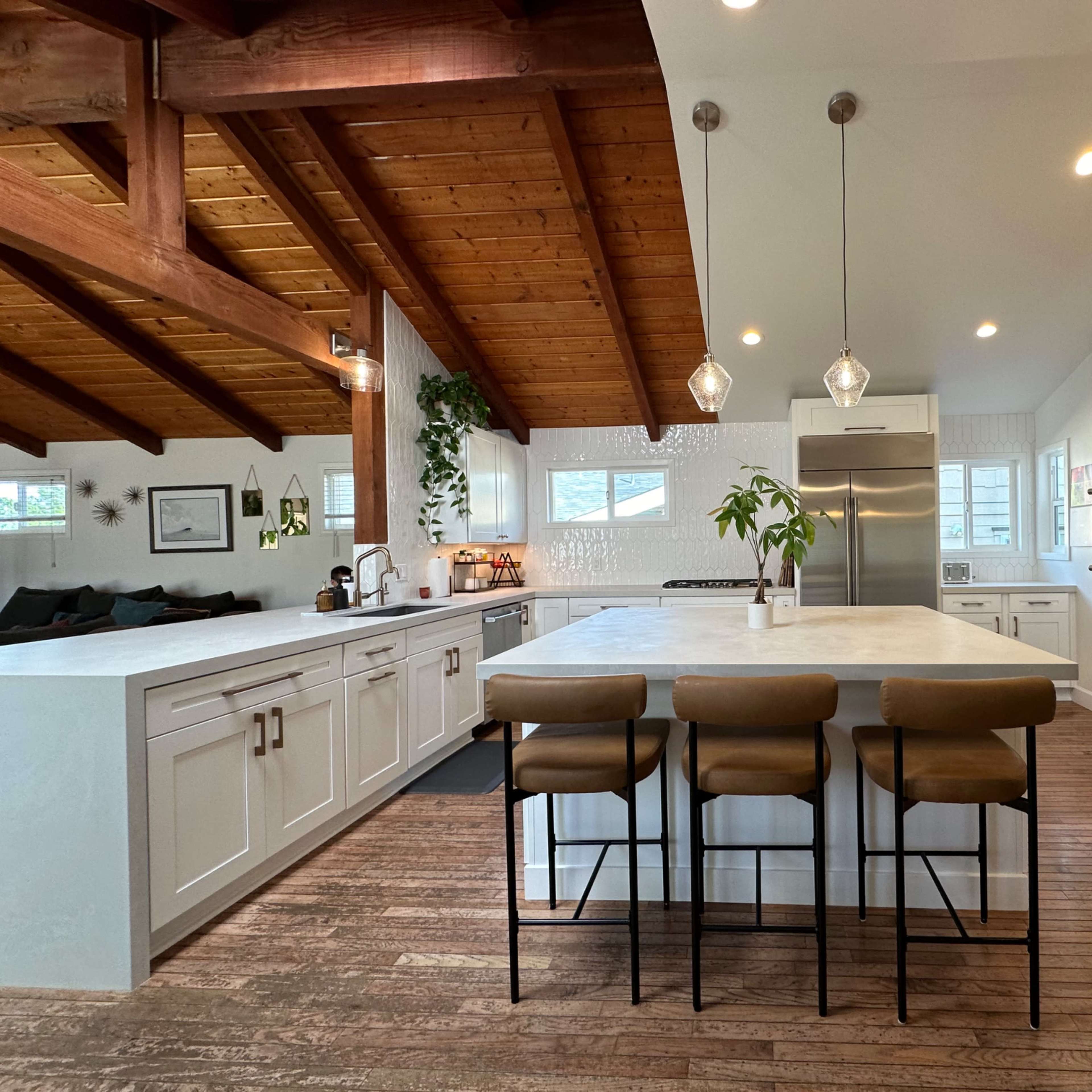 A spacious kitchen with wooden beams, an island with seating, modern appliances, and white cabinetry.