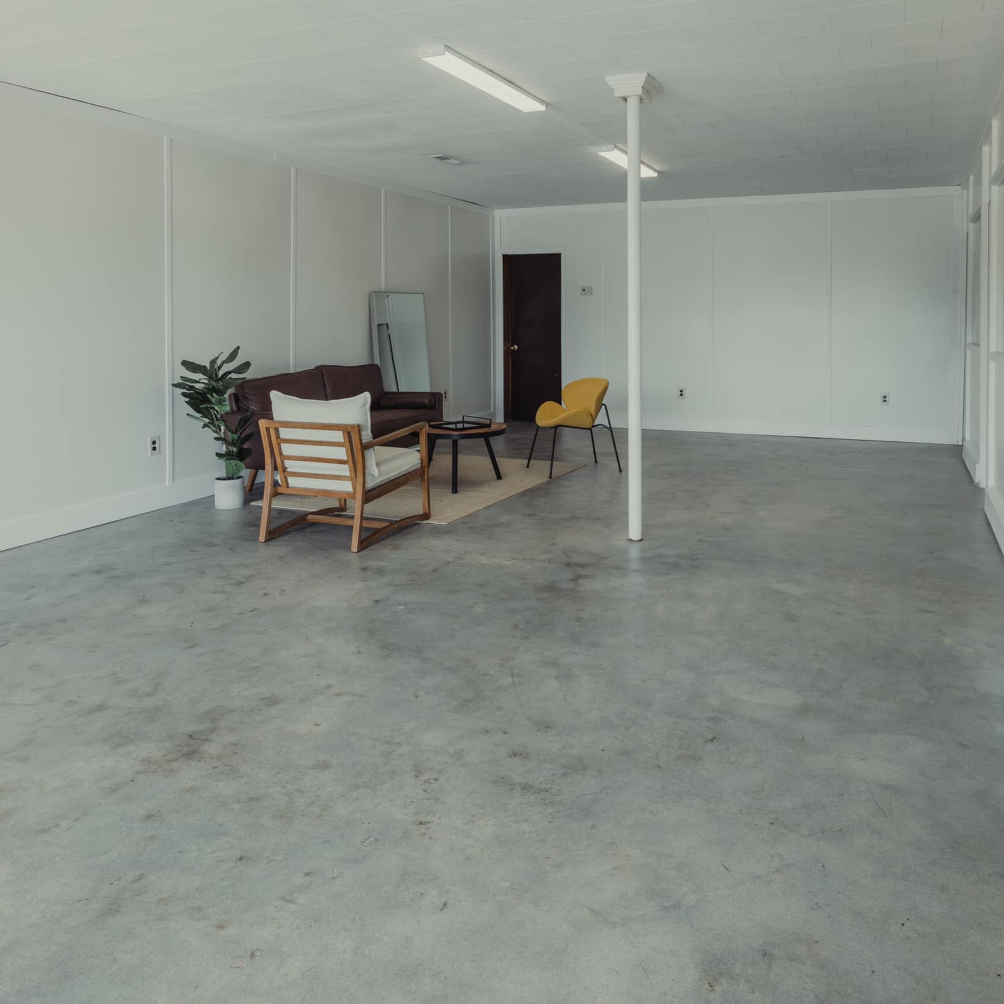 An empty room with a concrete floor featuring a sofa, a chair, a coffee table, and a plant in a corner.