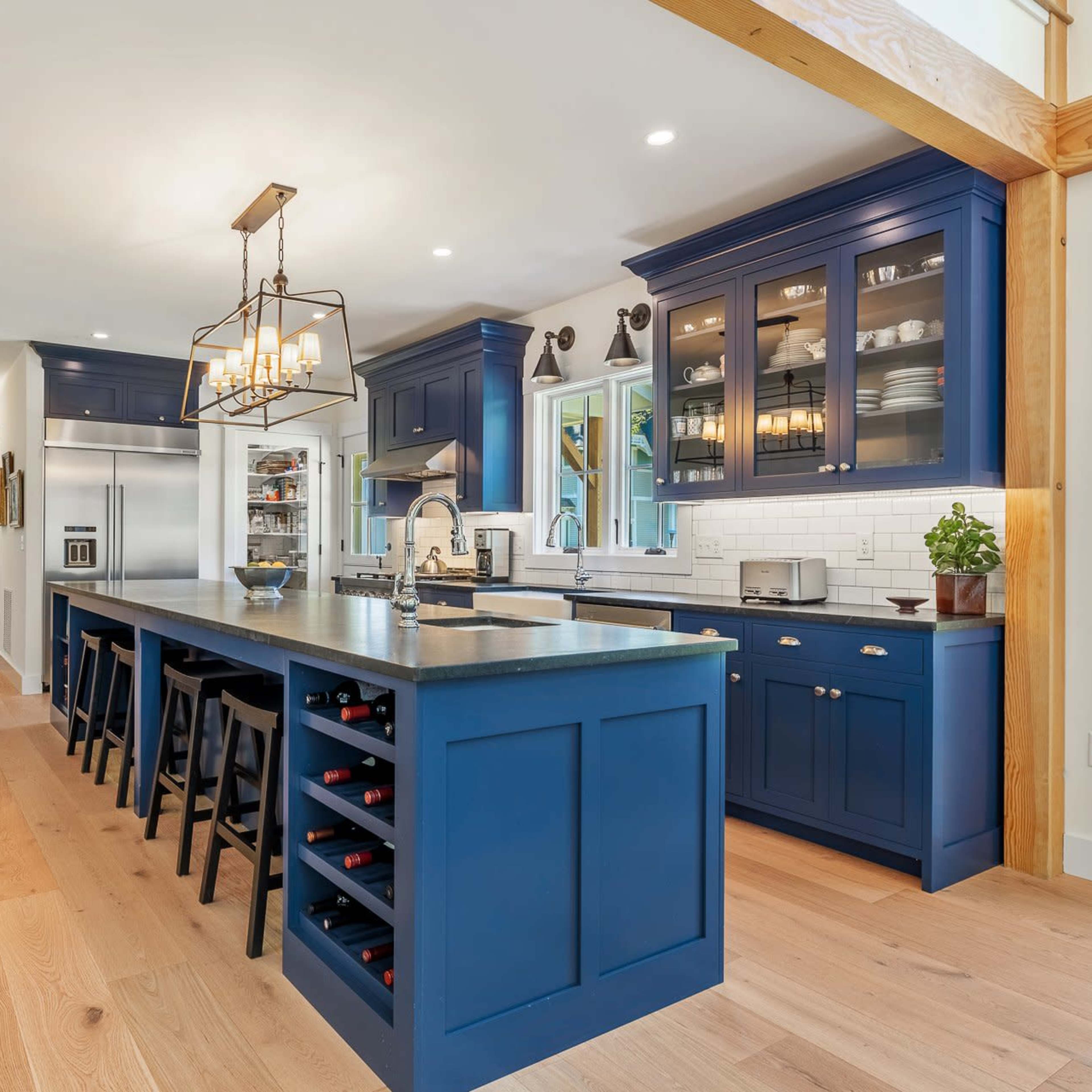 A modern kitchen features a blue island with seating, stainless steel appliances, and glass-front cabinets.