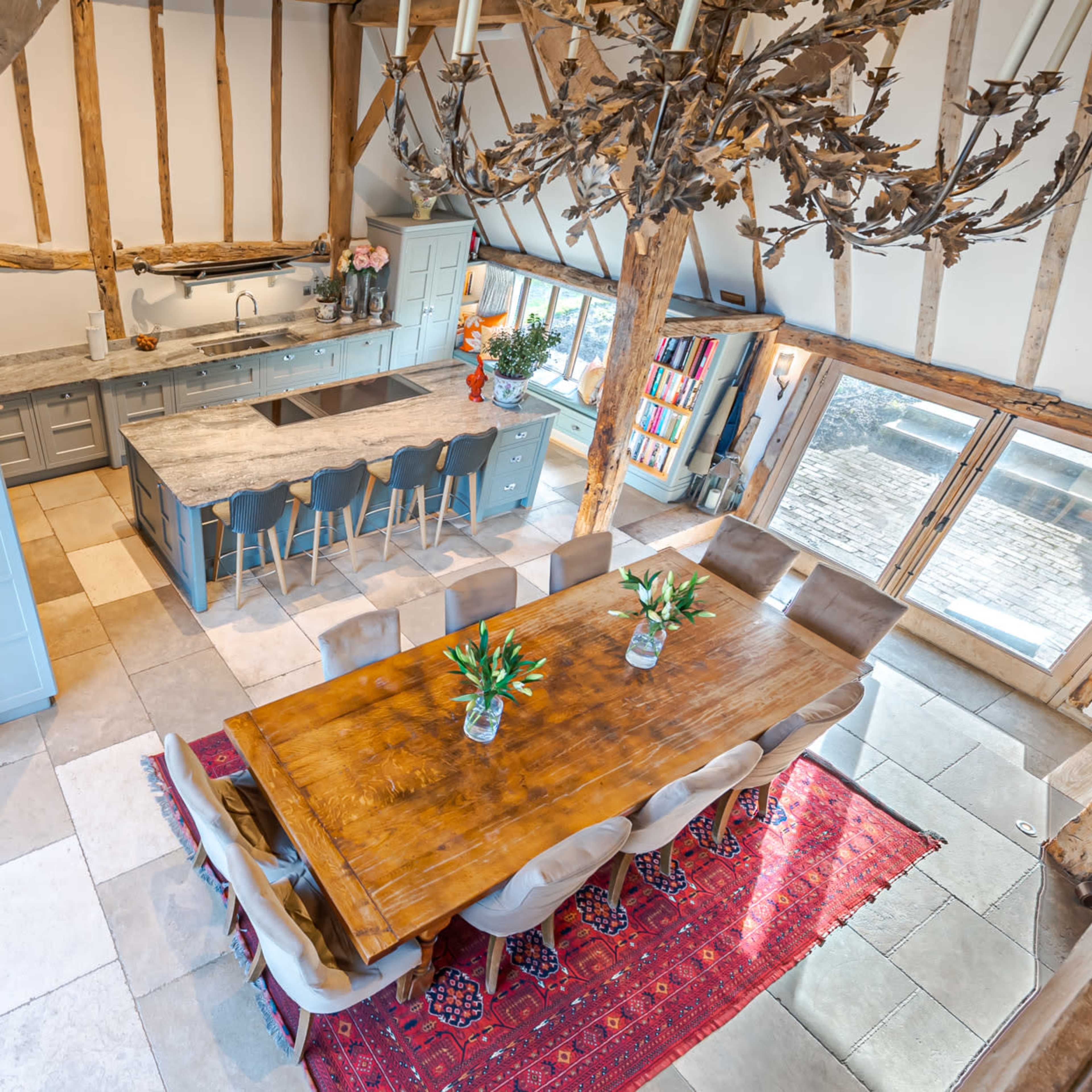 A spacious kitchen and dining area featuring a large wooden table surrounded by upholstered chairs, a gray kitchen island, and exposed timber beams.