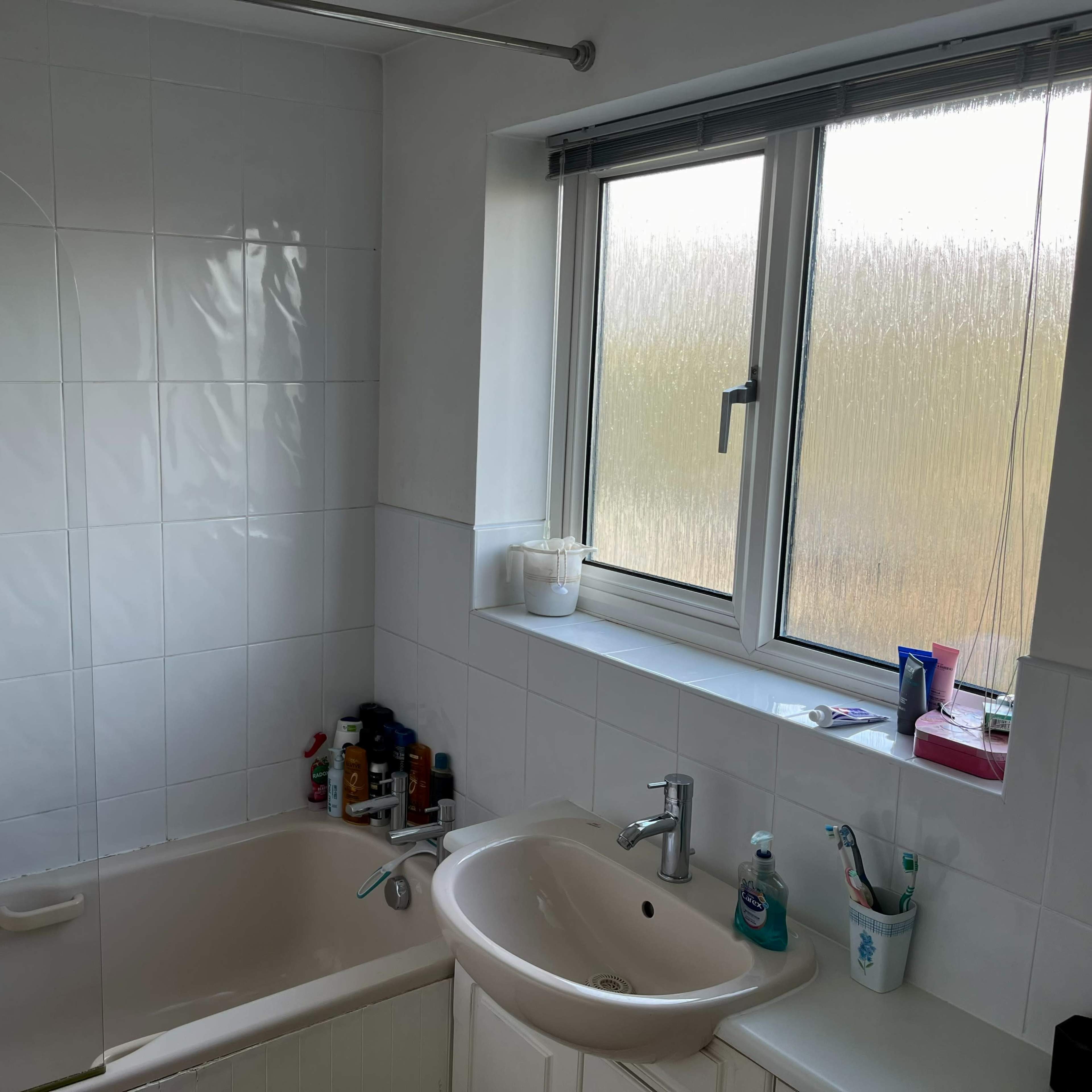 A bathroom with a bathtub, a wall-mounted sink, and a window partially covered with condensation.