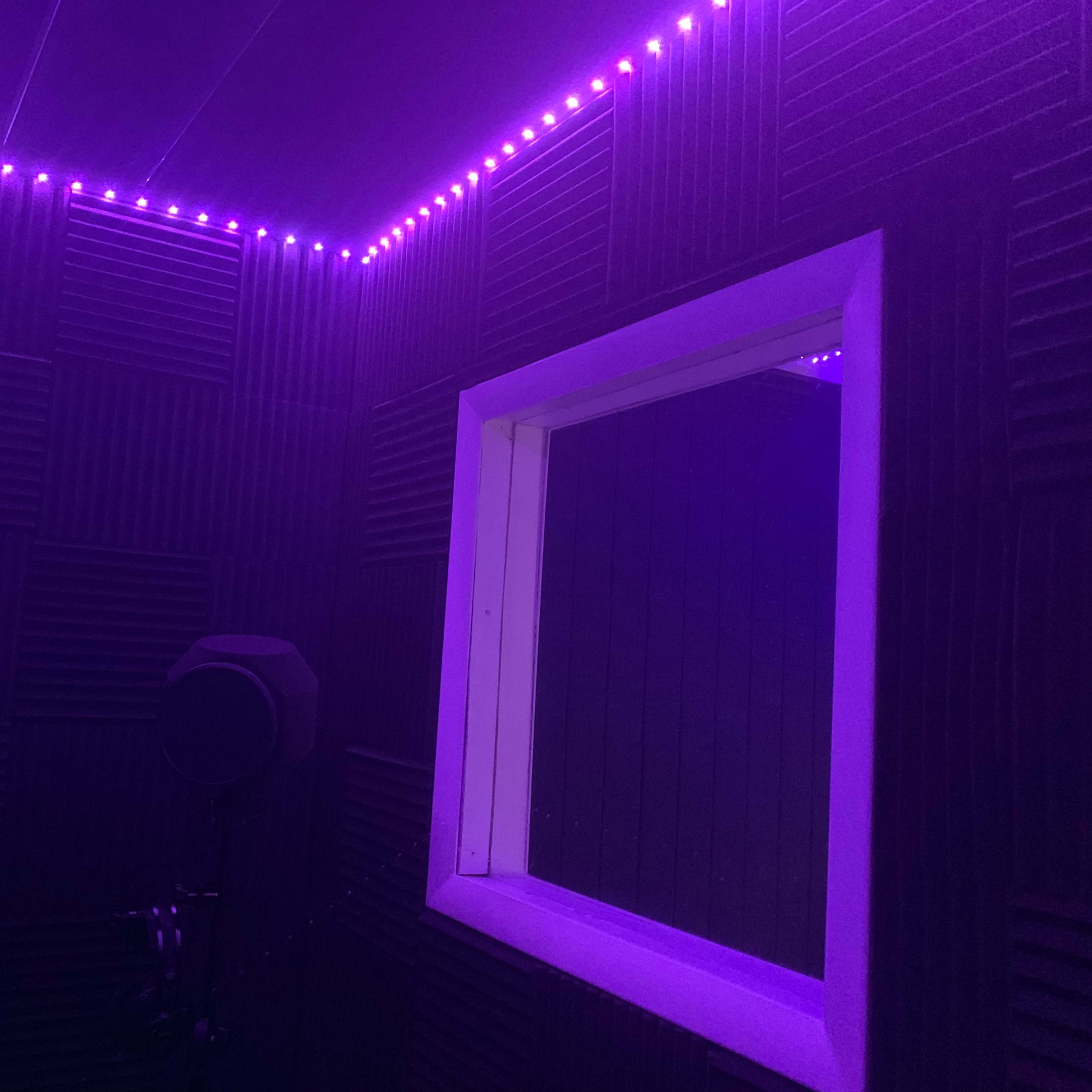 A soundproof recording booth with purple LED lighting and a window view.