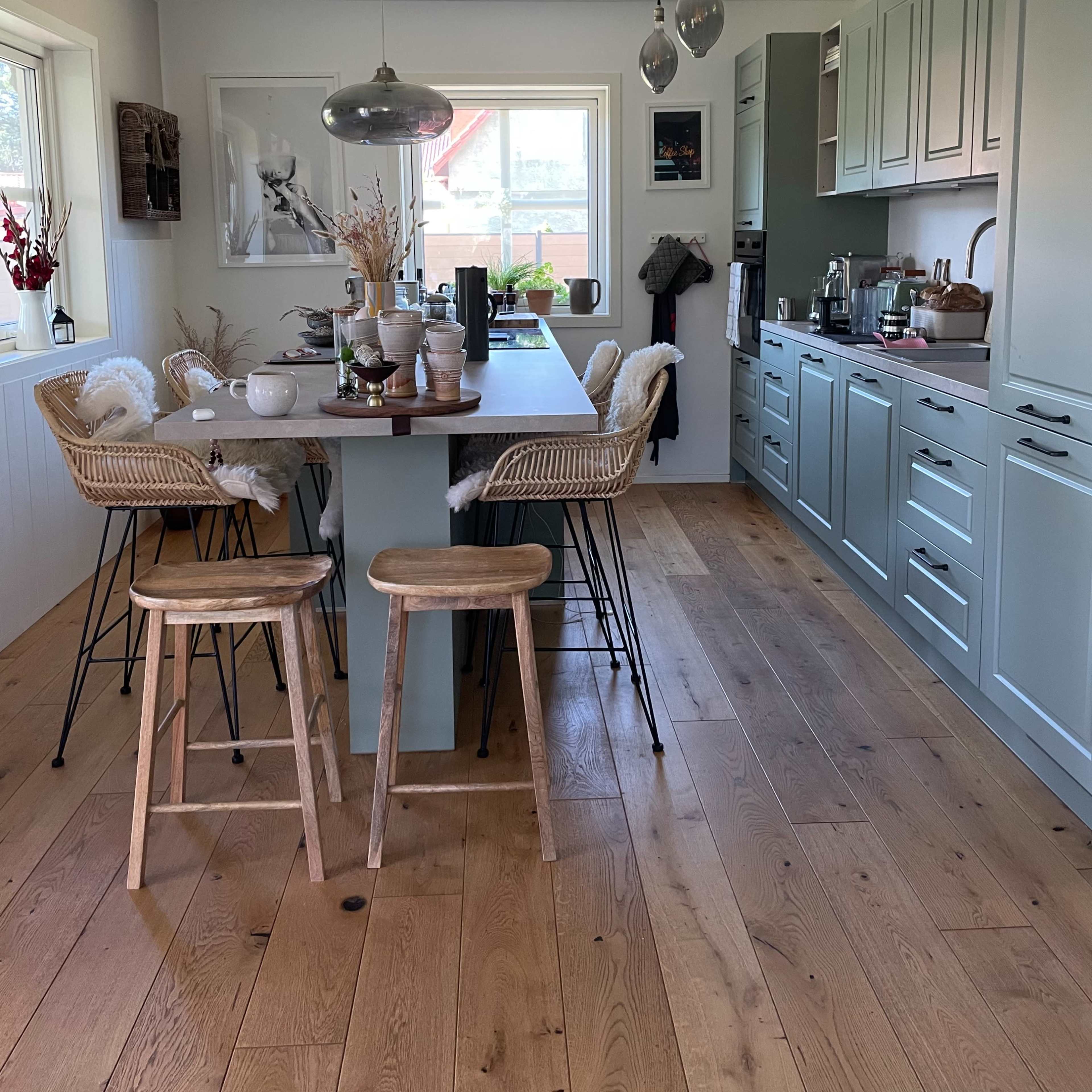 A modern kitchen features a table with three wooden stools, cabinetry with a soft blue finish, and pendant lighting above.