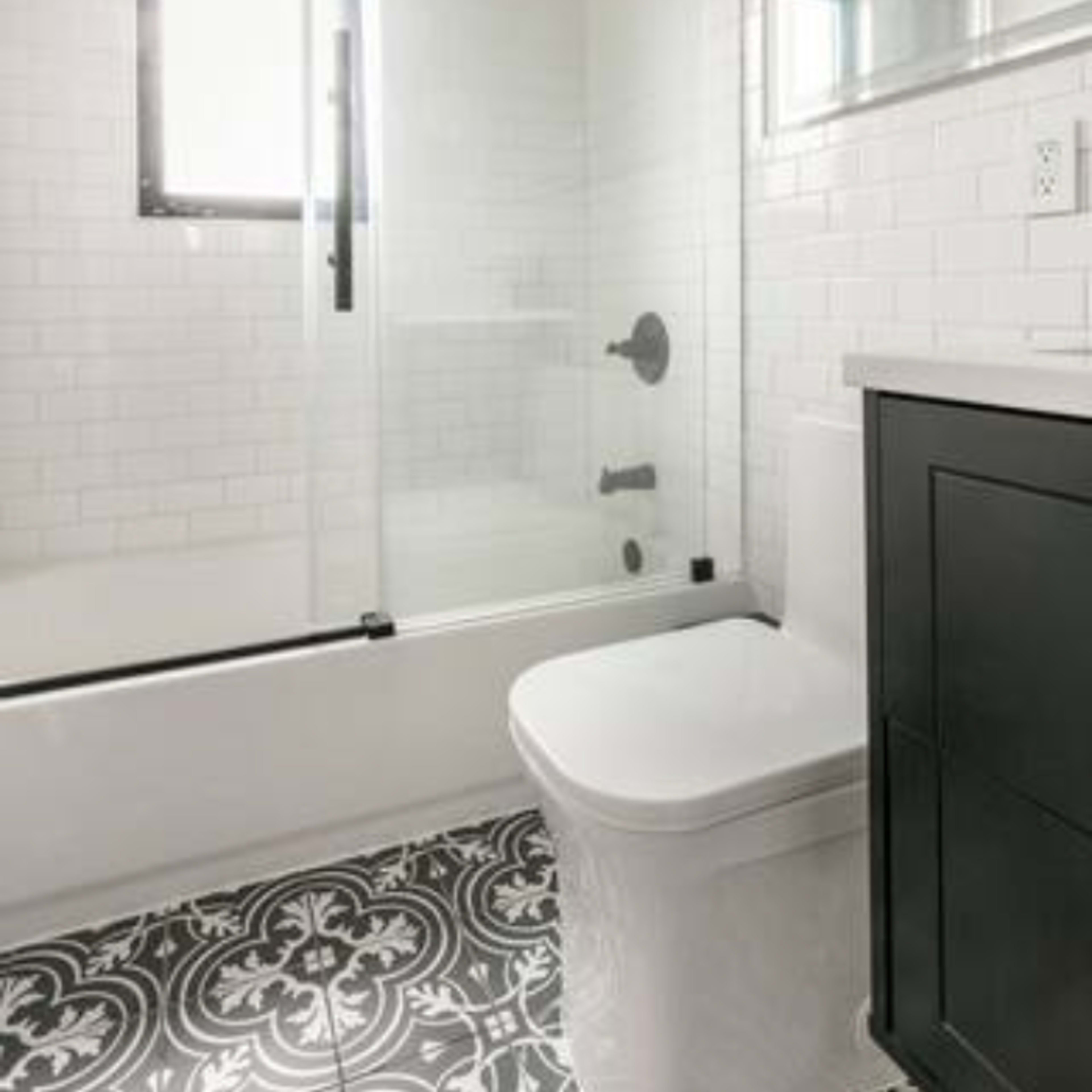 A modern bathroom featuring a glass shower enclosure, a white toilet, and patterned black-and-white floor tiles.