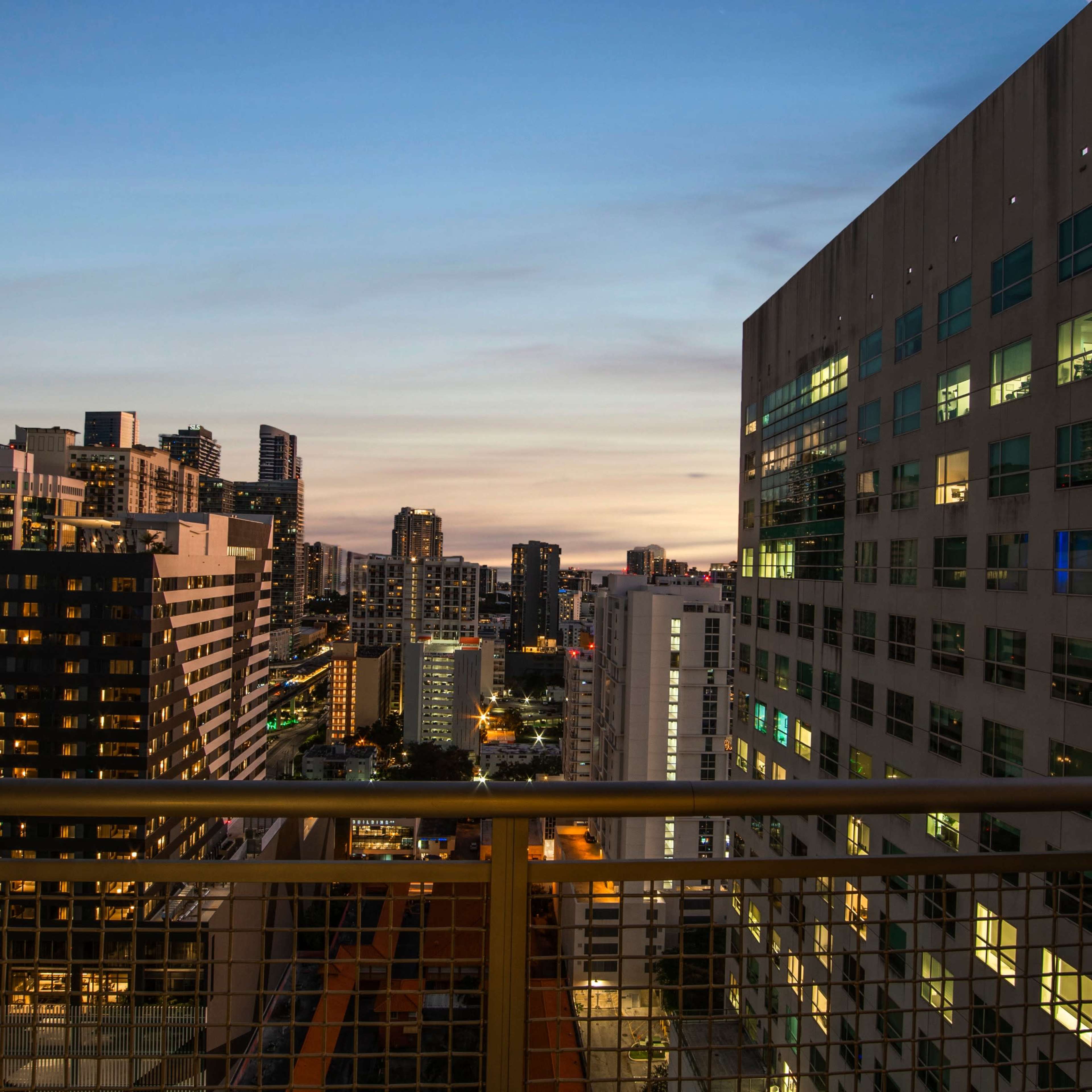 A city skyline at dusk, with tall buildings and illuminated windows against a colorful twilight sky.