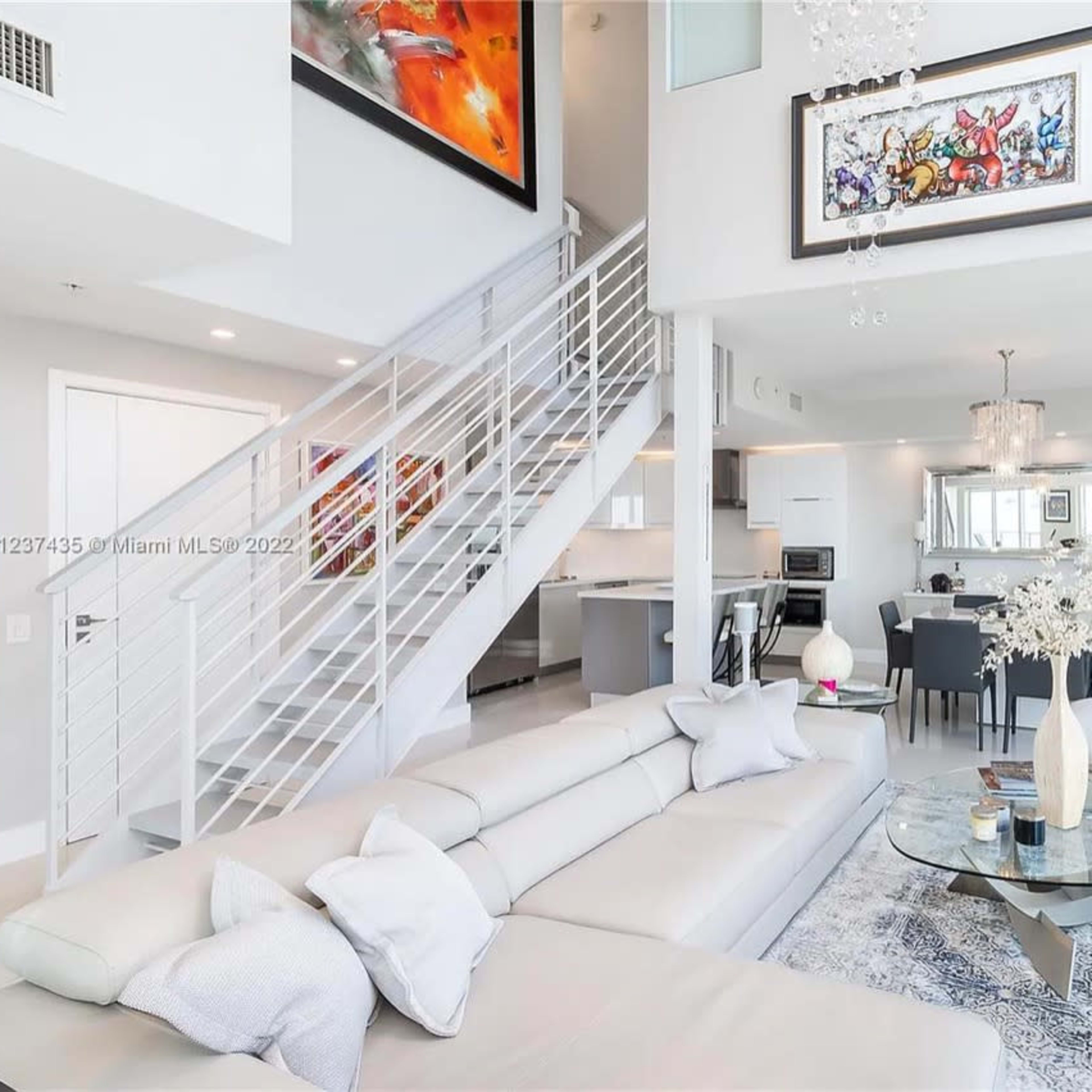 A modern, open-concept living area with a large sectional sofa, a glass coffee table, and a dining space adjacent to a sleek kitchen.