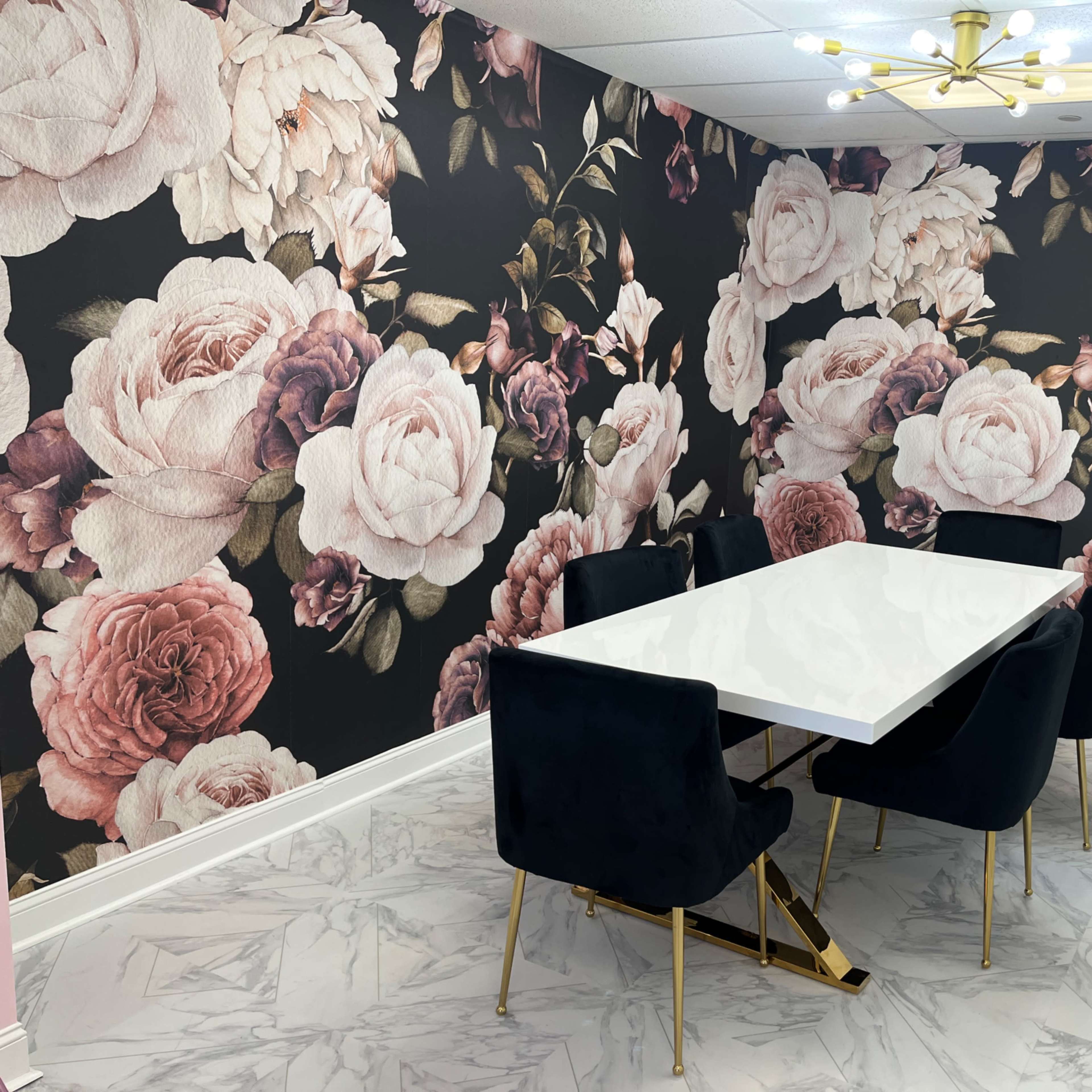 A meeting room features a white table surrounded by black chairs, with a floral wallpaper design displaying large pink and burgundy roses.