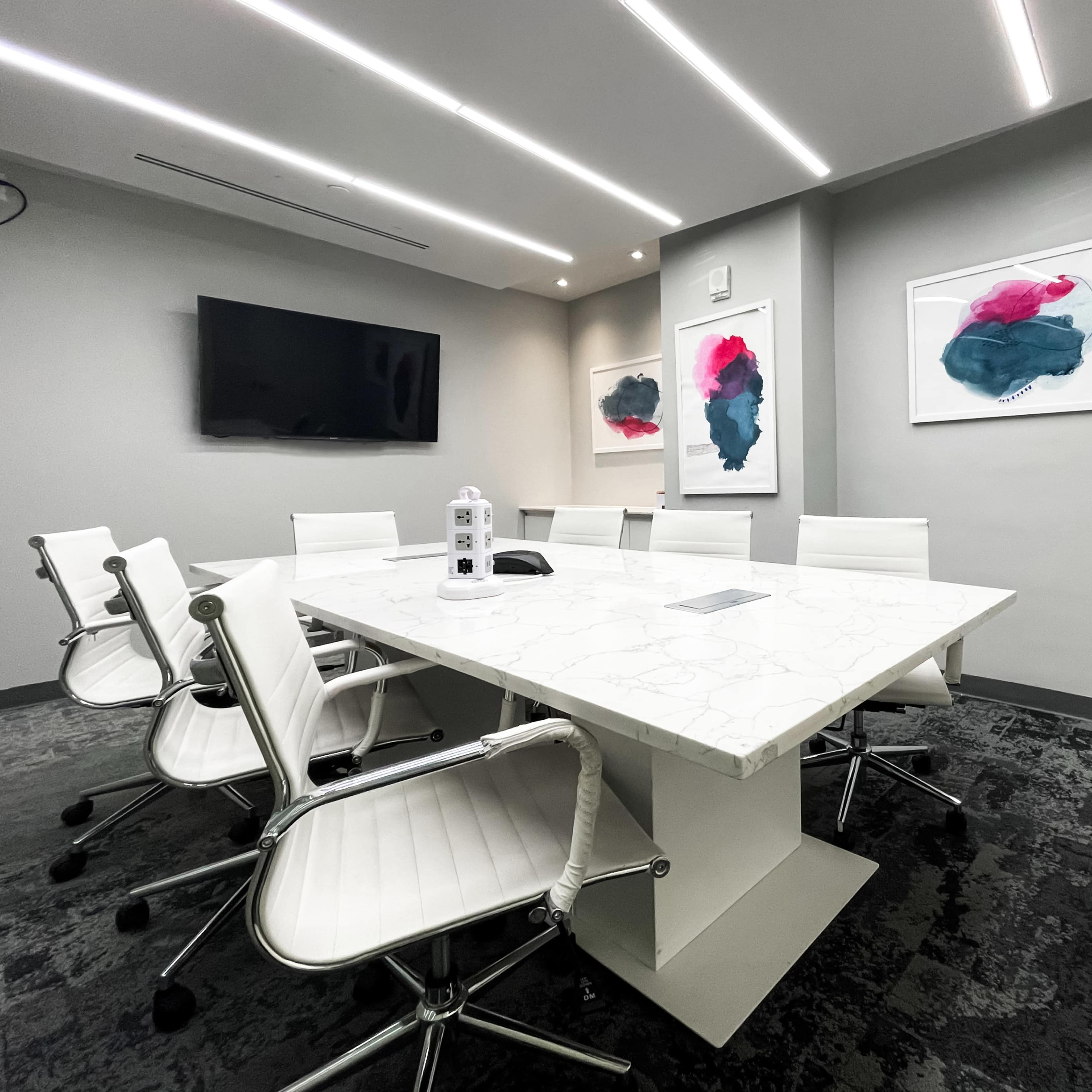 A modern conference room features a white marble table, six white chairs, and two abstract artworks on the walls.