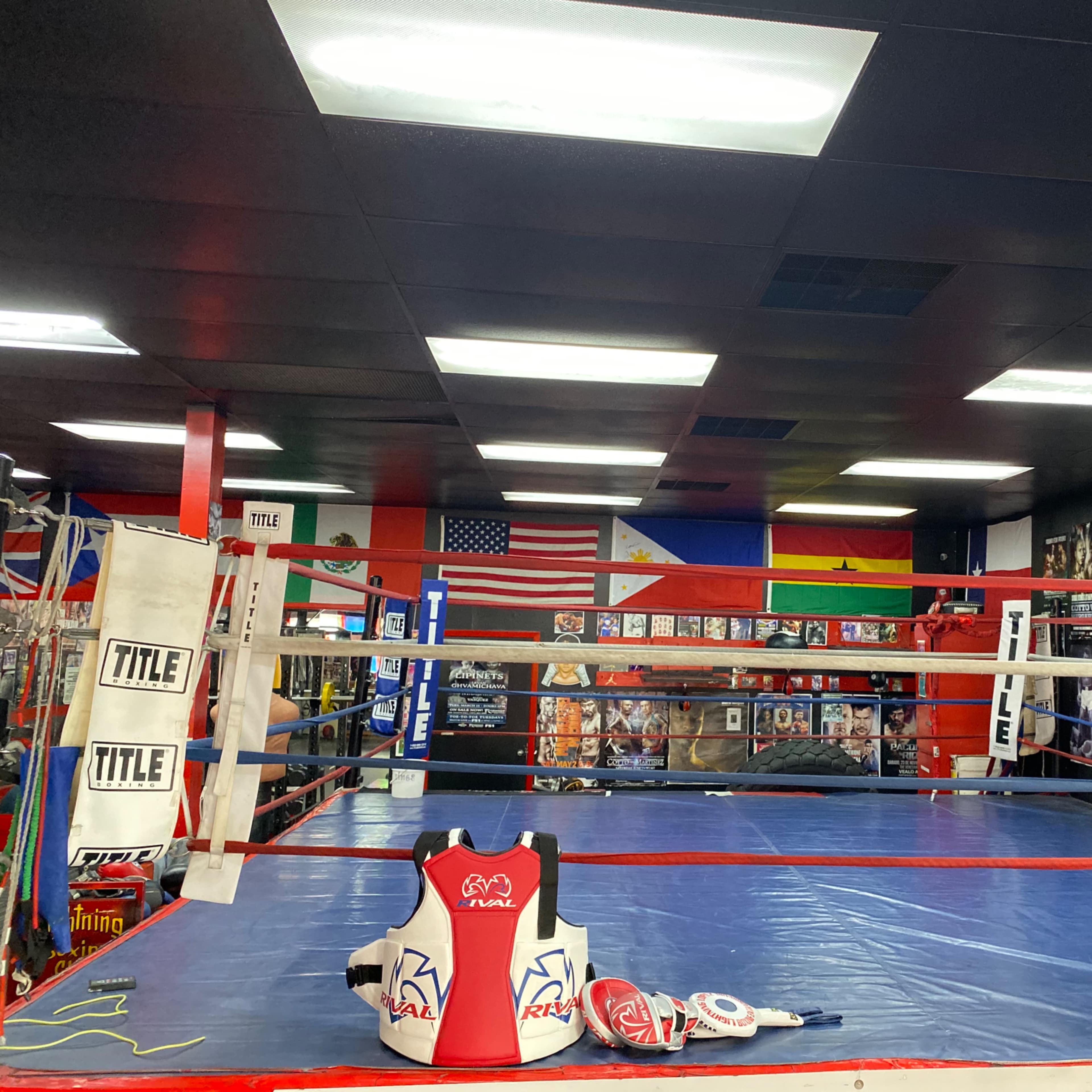 A boxing ring in a gym, surrounded by various flags and posters on the walls.