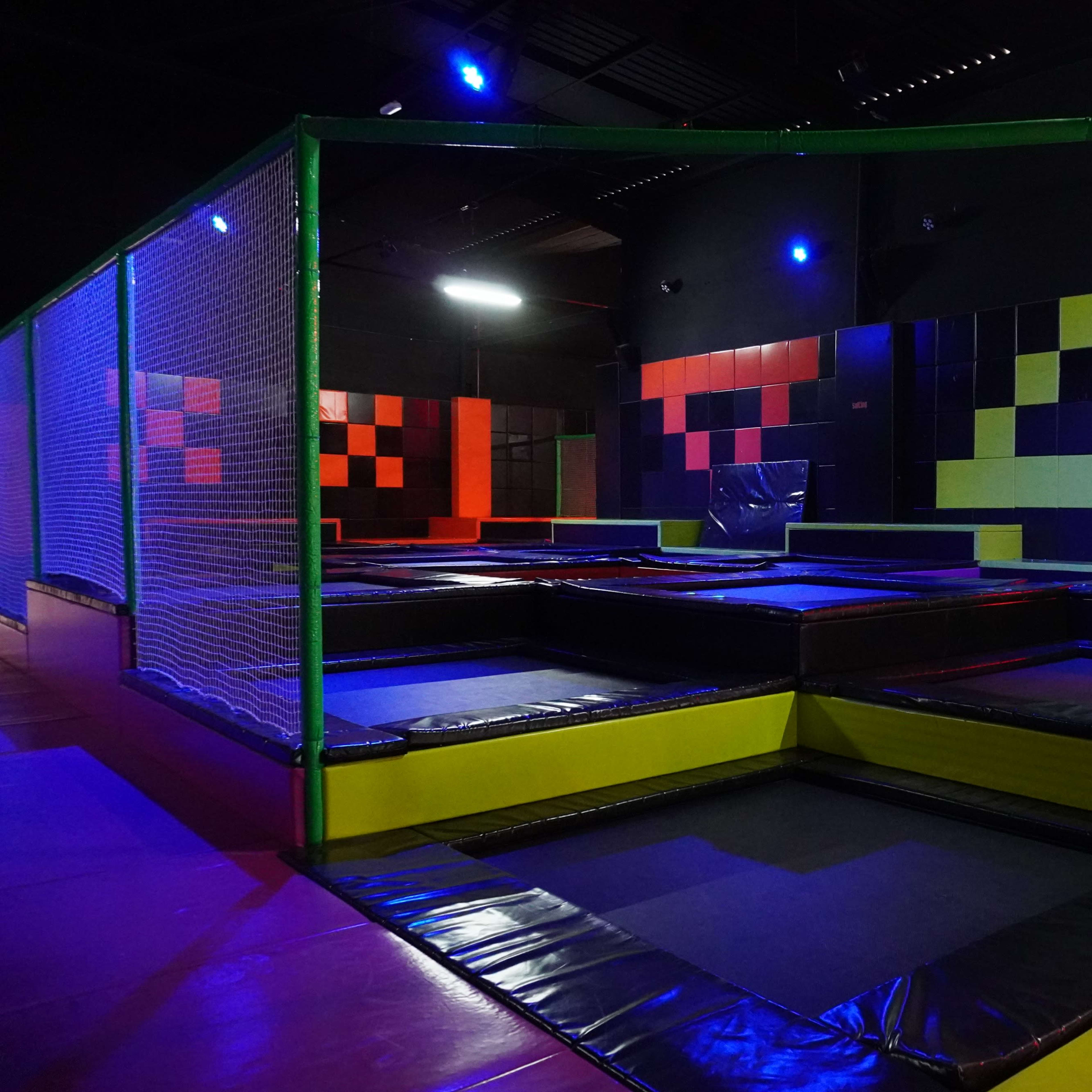 An indoor trampoline park with multiple trampoline areas enclosed by safety nets and colorful wall panels.