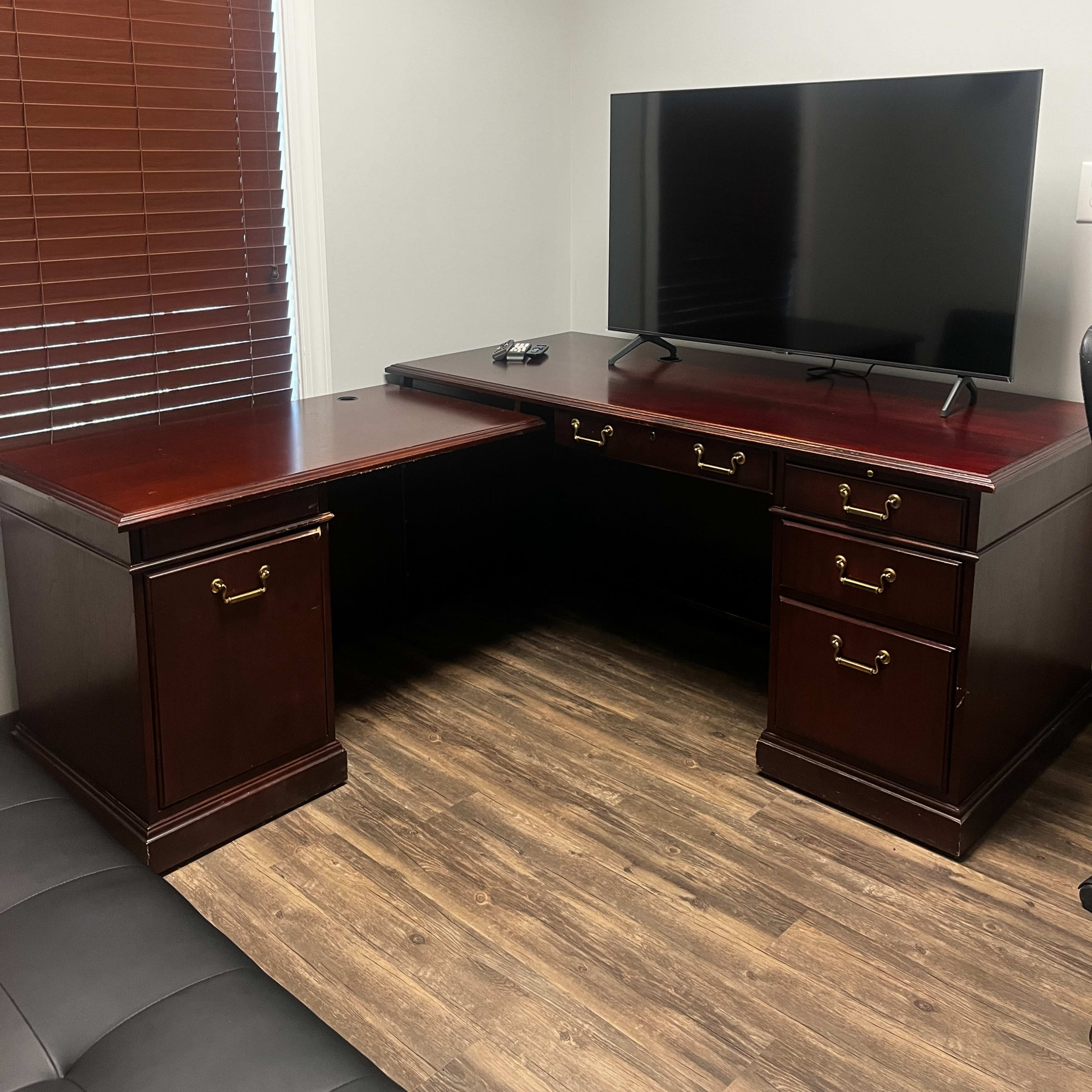 A corner office setup featuring a dark wooden desk with drawers and a television mounted on the wall above it.