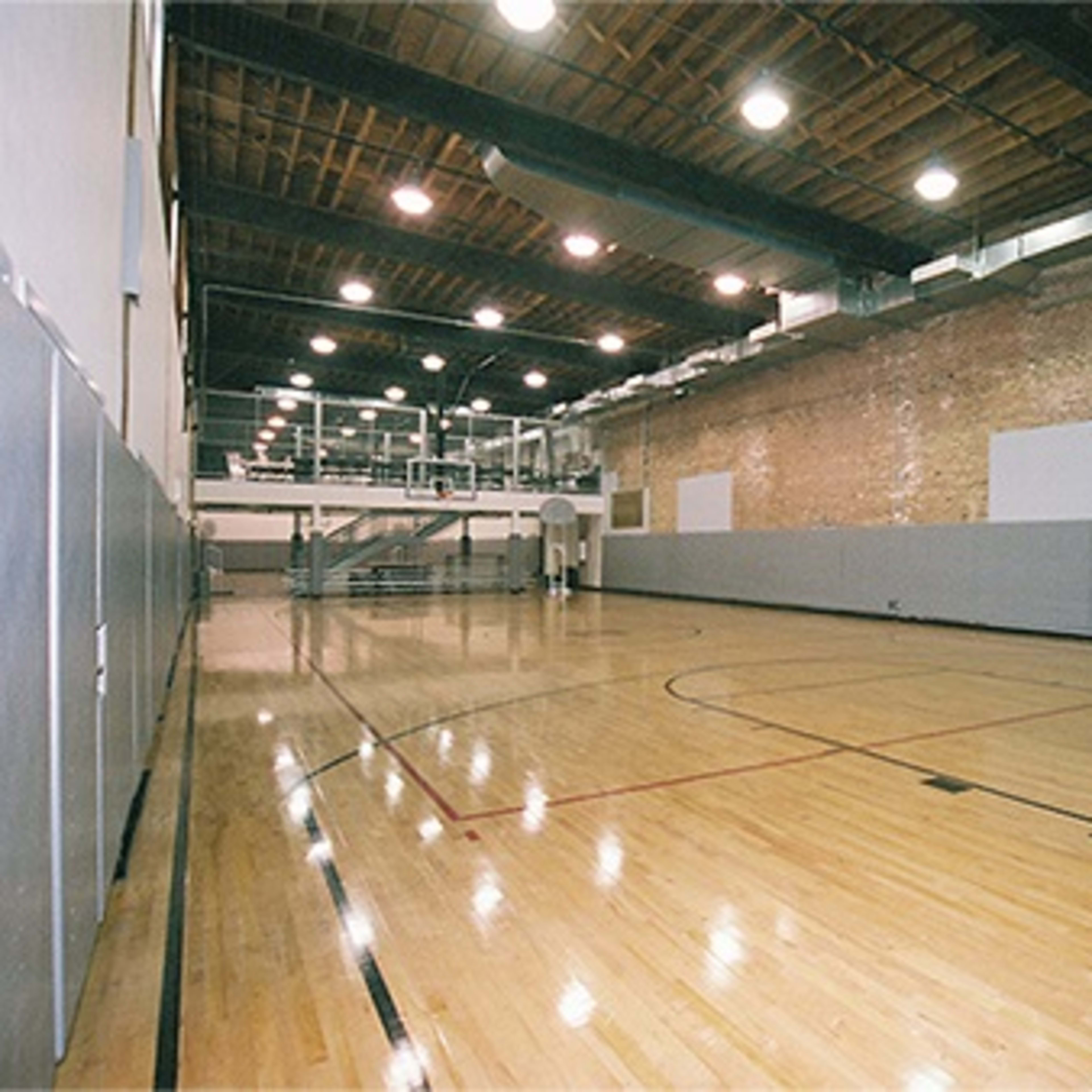 A spacious indoor basketball court with hardwood flooring, a hoop at one end, and padded walls along the sides.