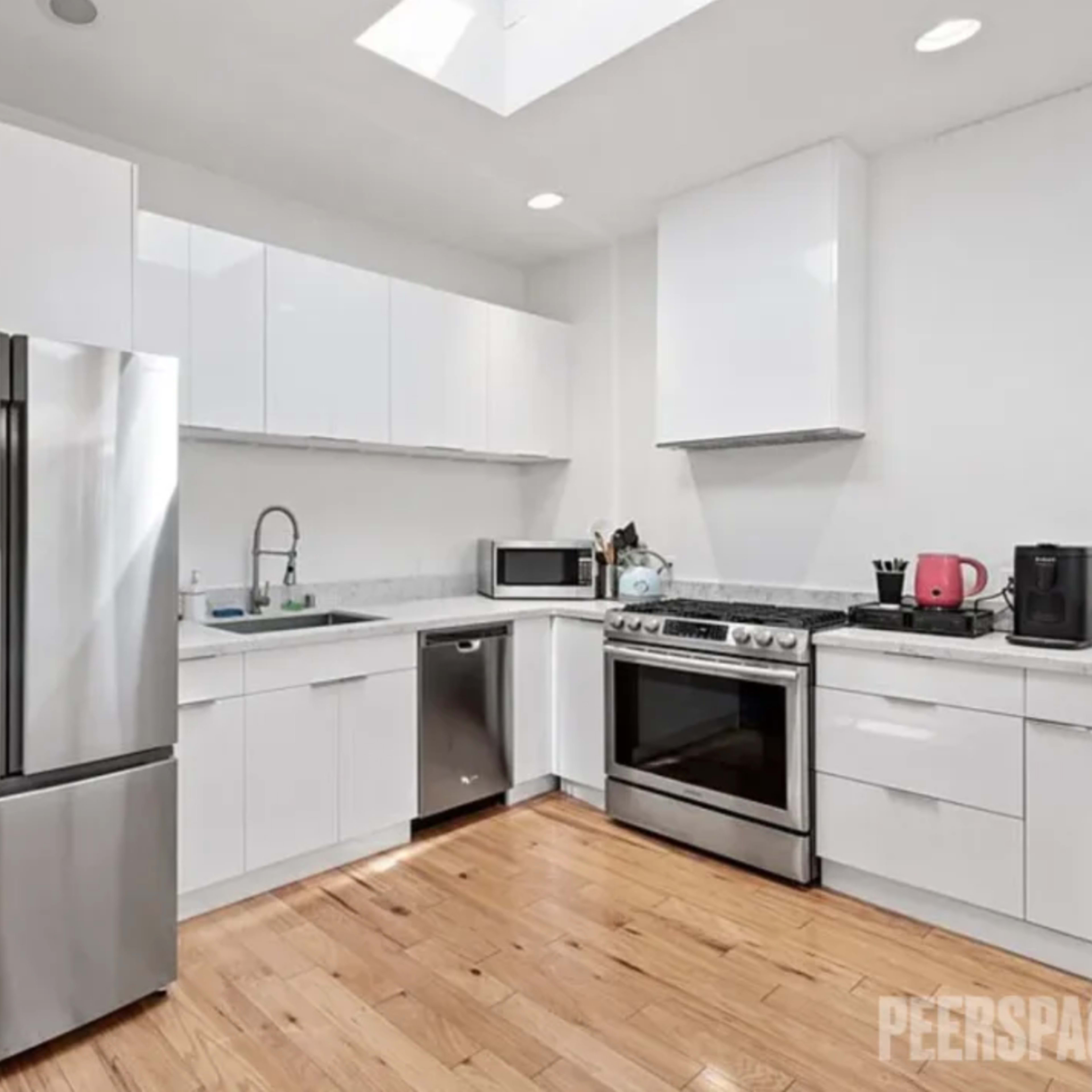 A modern kitchen with stainless steel appliances, white cabinetry, and a wooden floor.