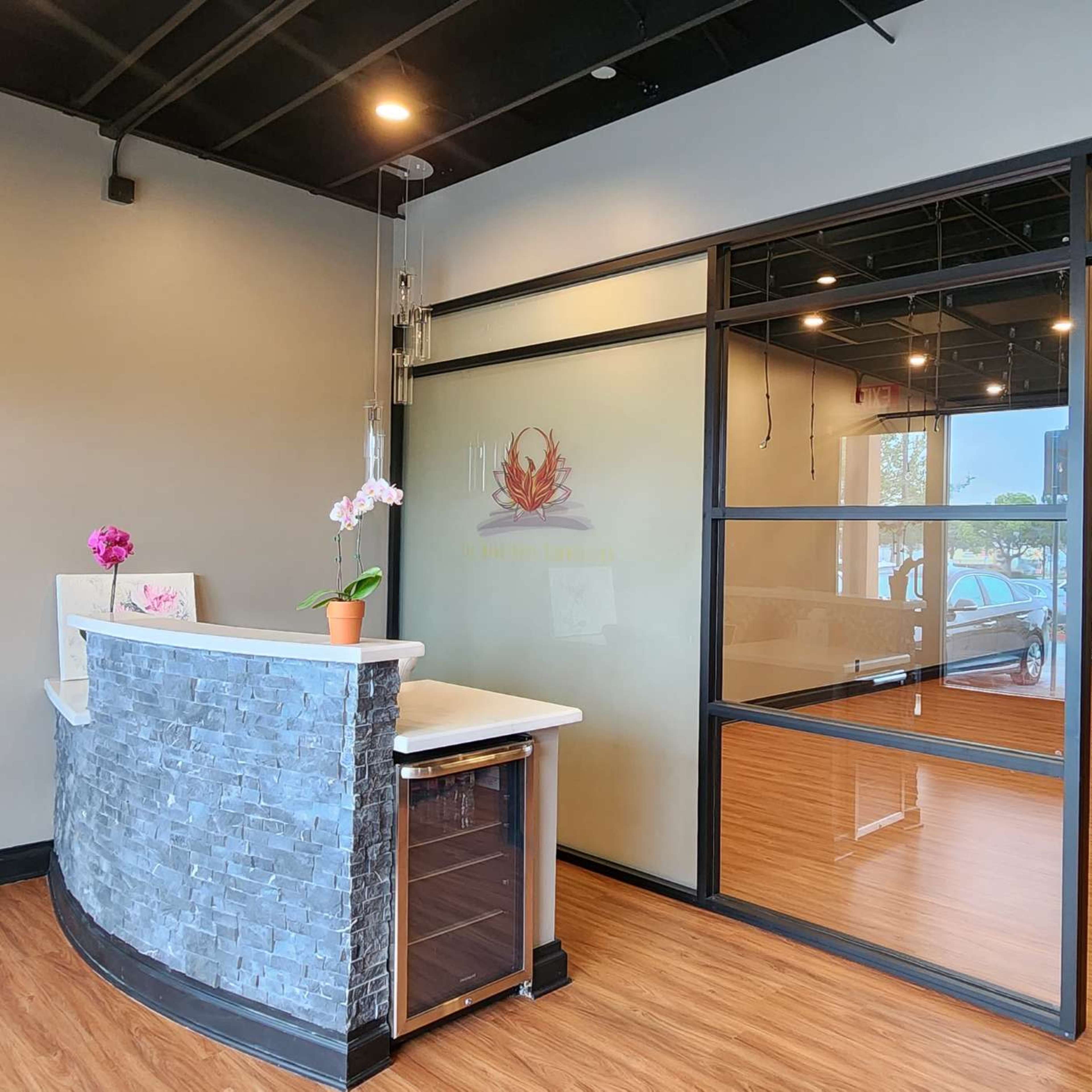 A modern reception area with a stone front desk, a potted orchid, and large glass panels leading into a spacious room with wooden flooring.