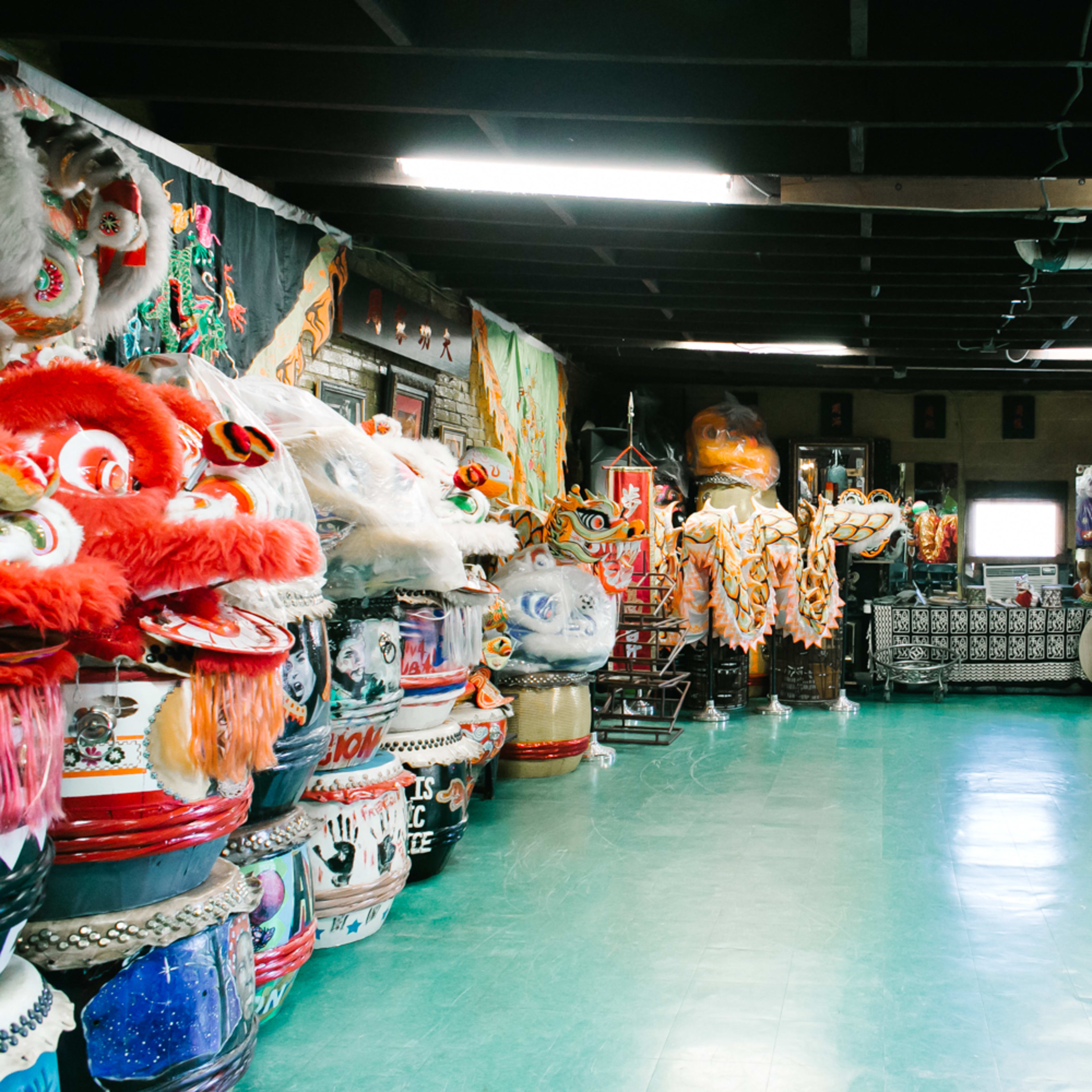 A spacious room filled with colorful traditional costumes, large lion dance heads, and various props lined along the walls.
