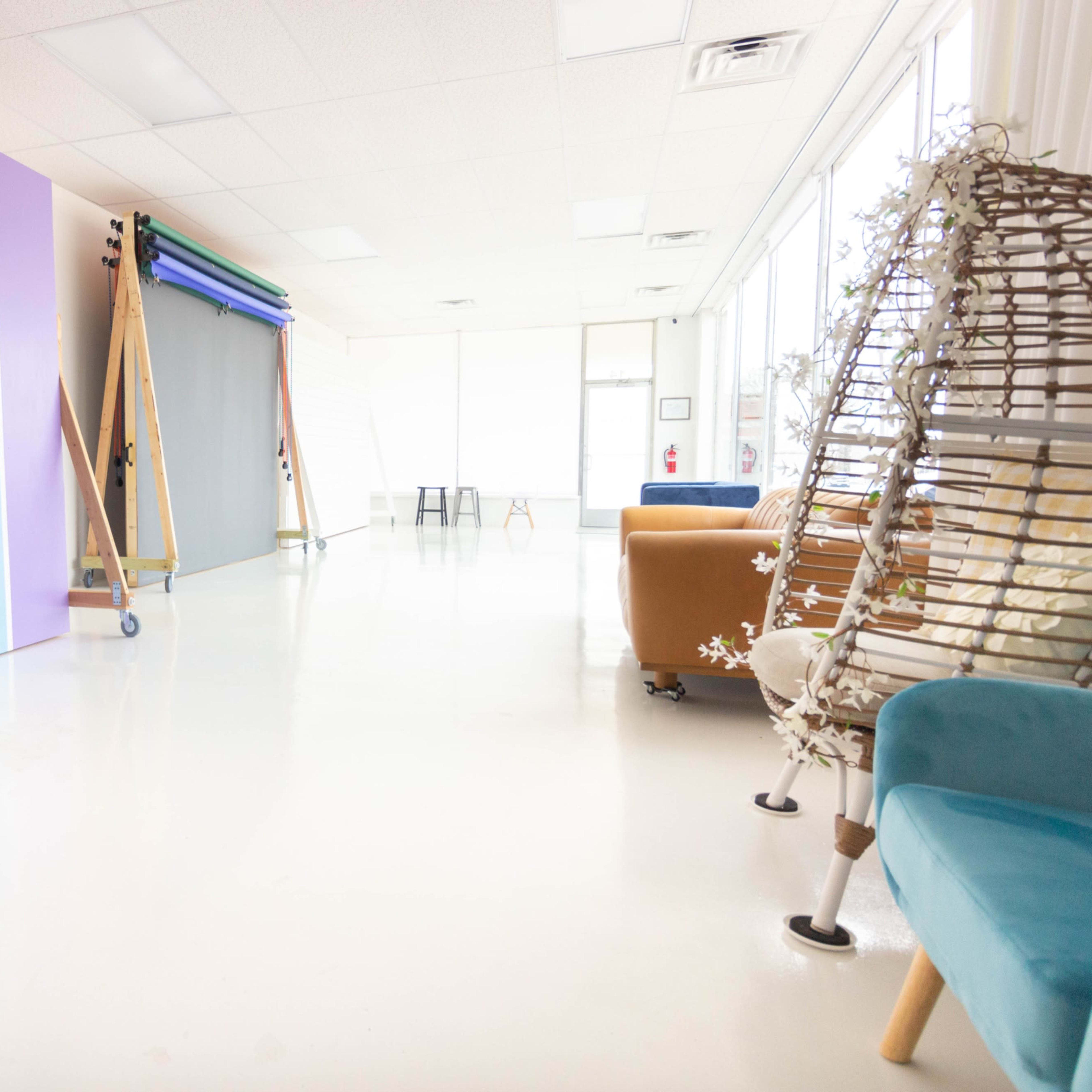 A well-lit studio space featuring colorful backdrop panels, a photography backdrop stand, and a mix of modern seating arrangements.