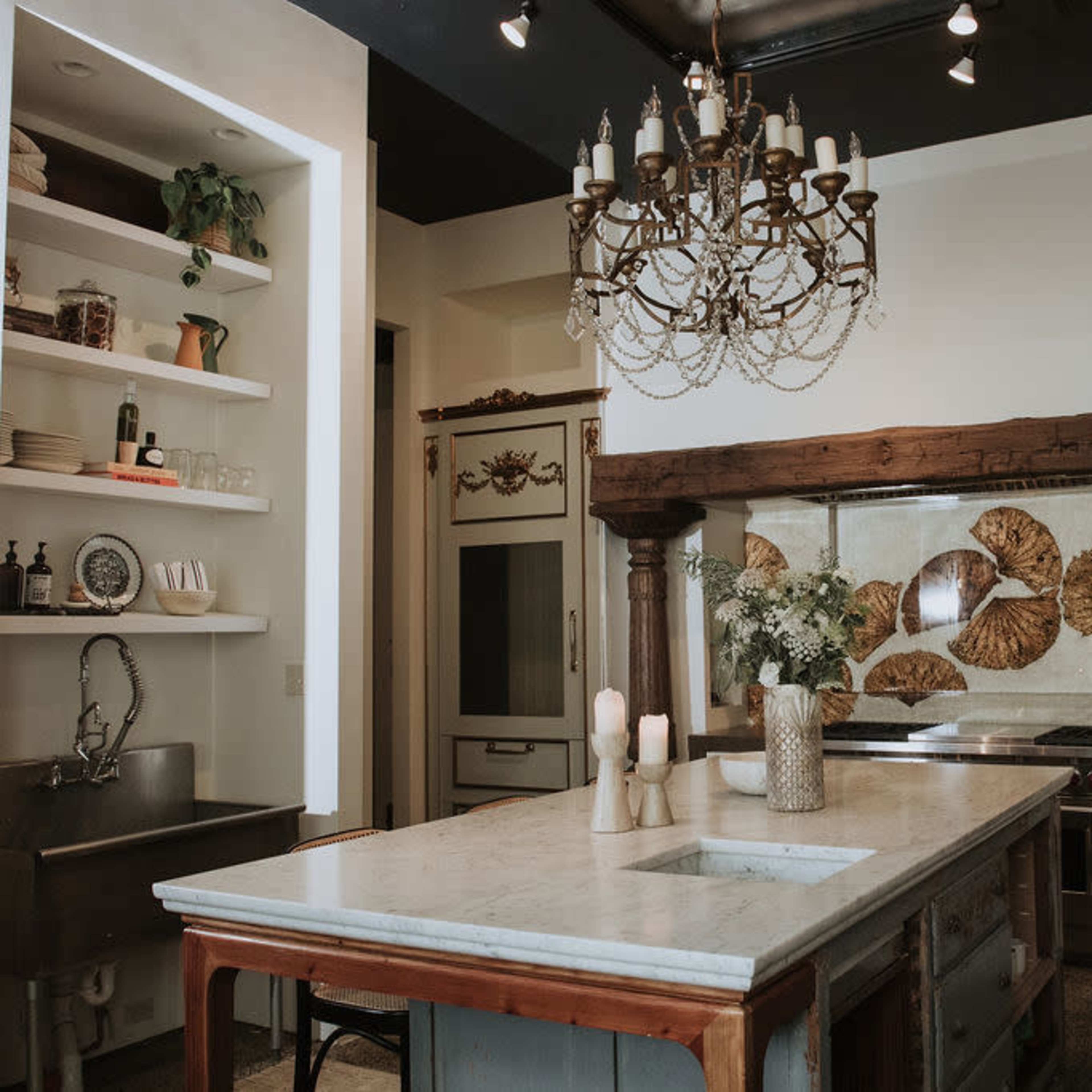 A spacious kitchen featuring a marble island, a decorative chandelier, and wooden accents with a sink and open shelving.