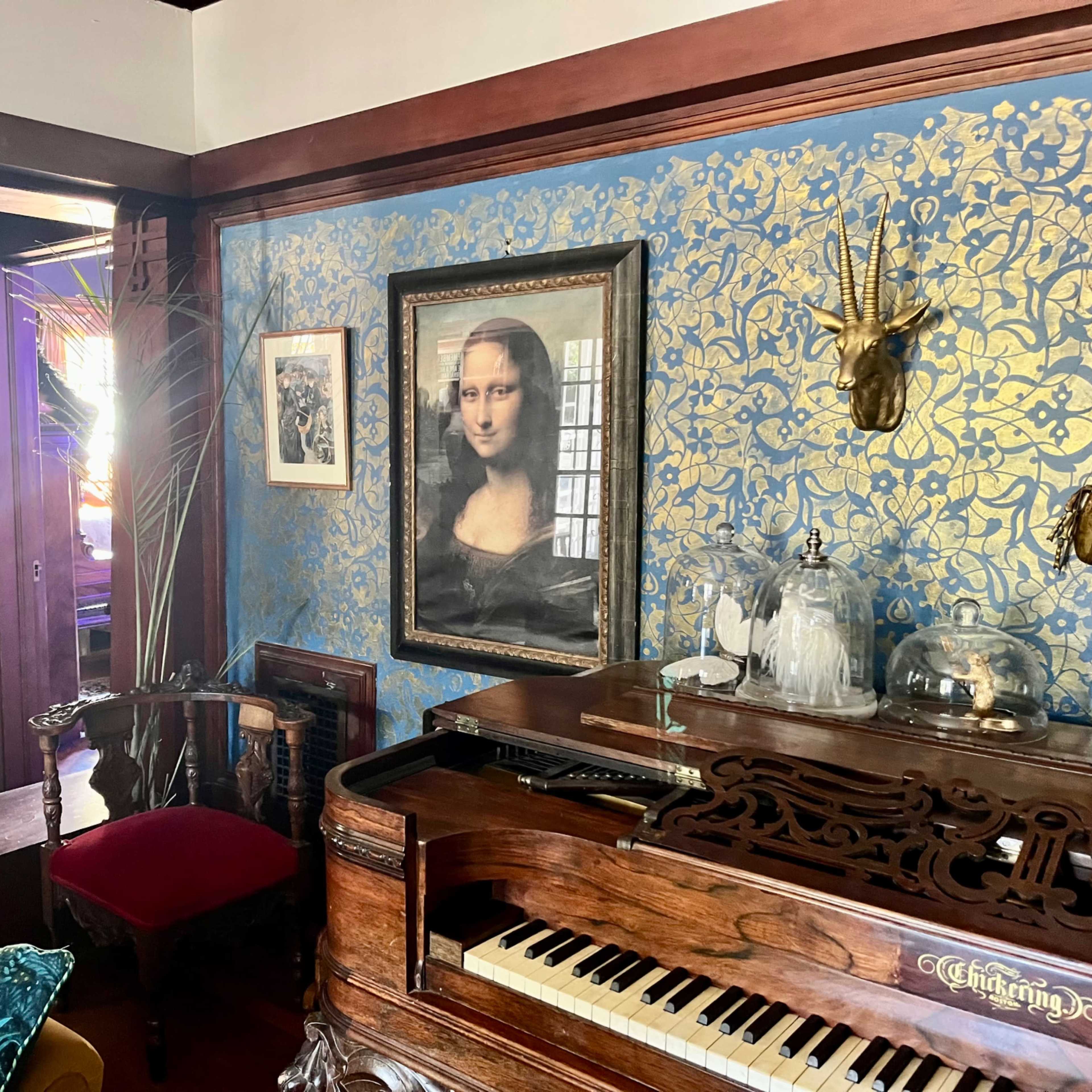 The scene features a room with a grand piano, a portrait of the Mona Lisa on a blue and gold patterned wall, and wooden furnishings, including a chair and a couch.