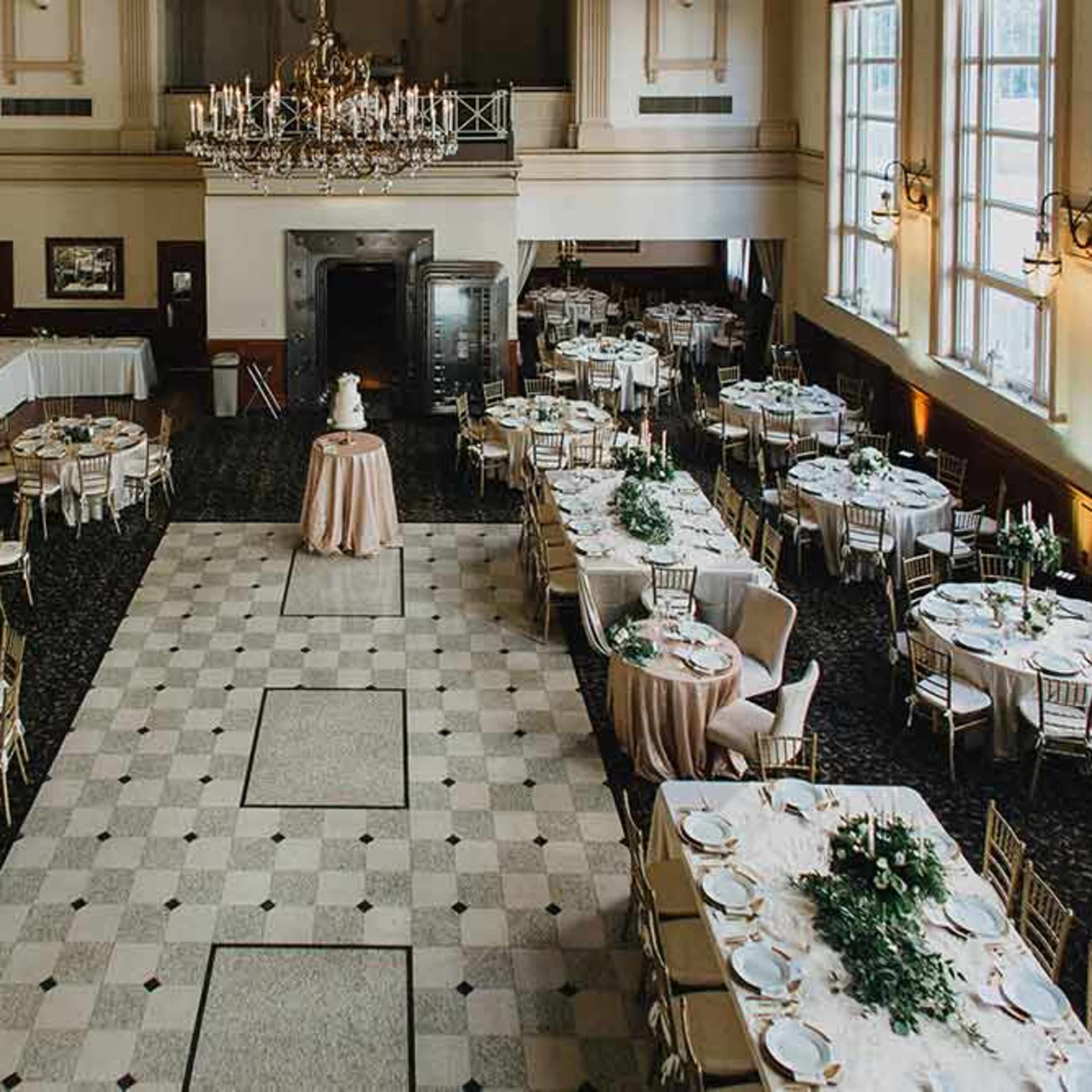 A banquet hall arranged with neatly set tables and a central cake display under a chandelier.