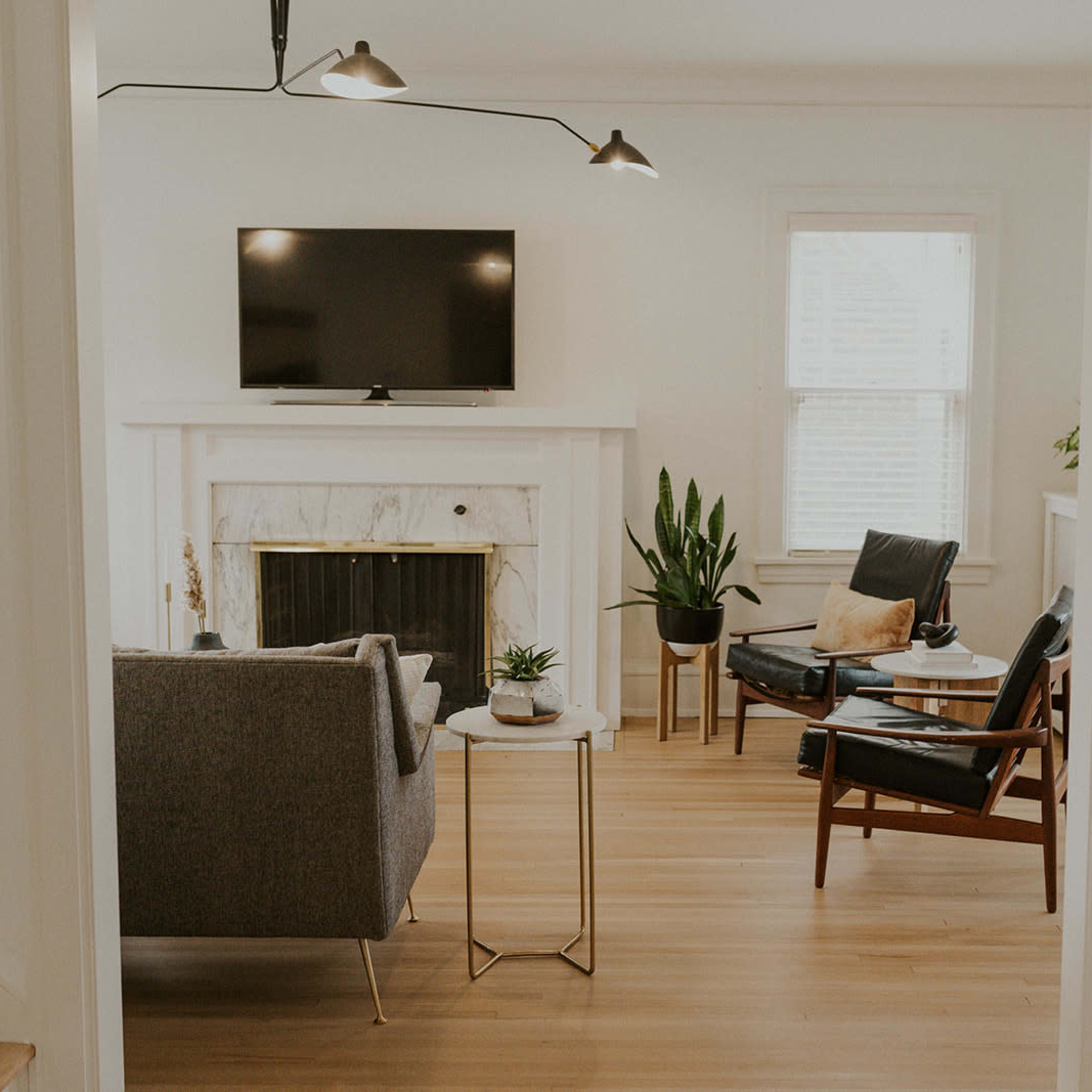 A modern living room features a gray sofa, a wooden chair, a marble fireplace, and a television mounted on the wall.