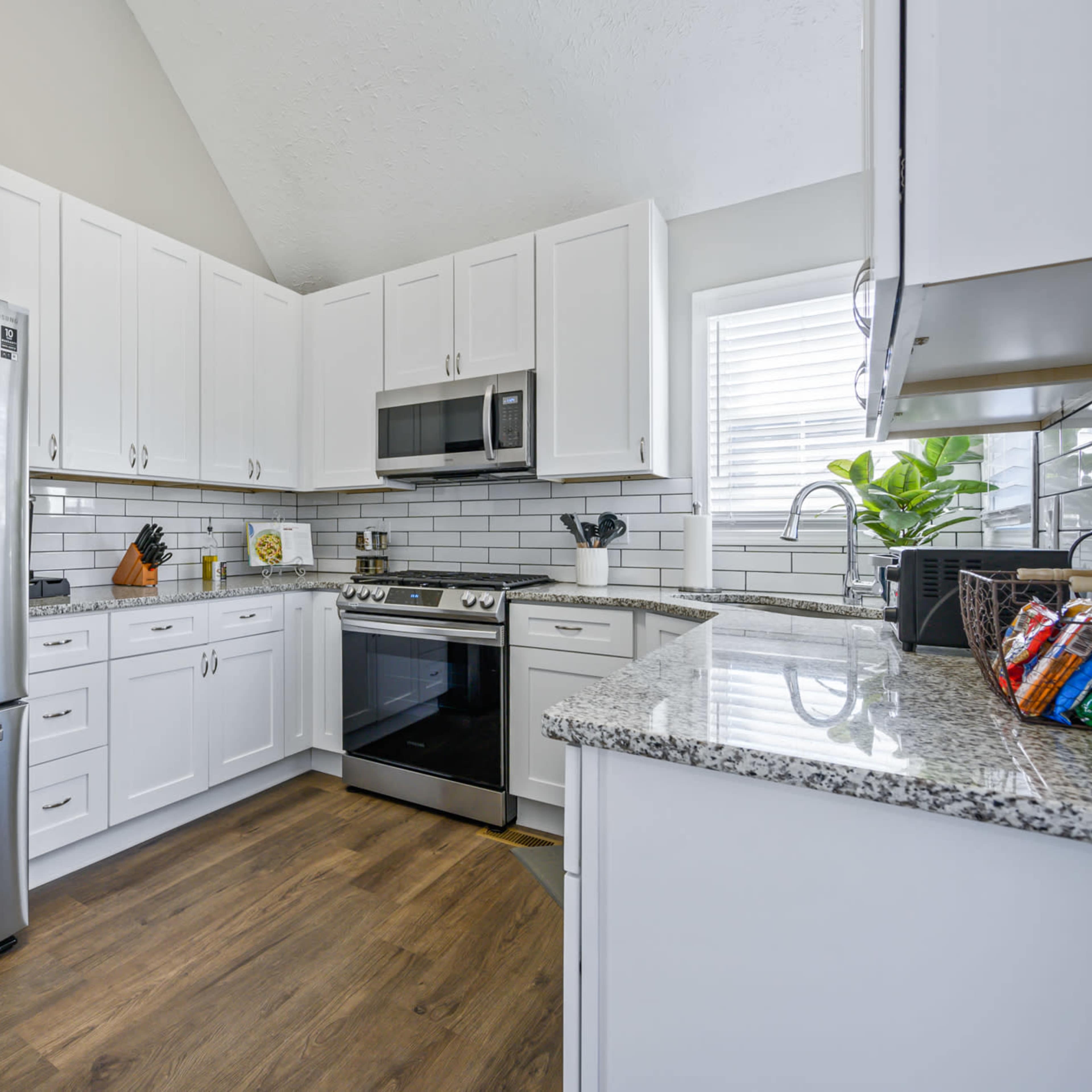 A modern kitchen features stainless steel appliances, white cabinetry, and a granite countertop with a wood floor.