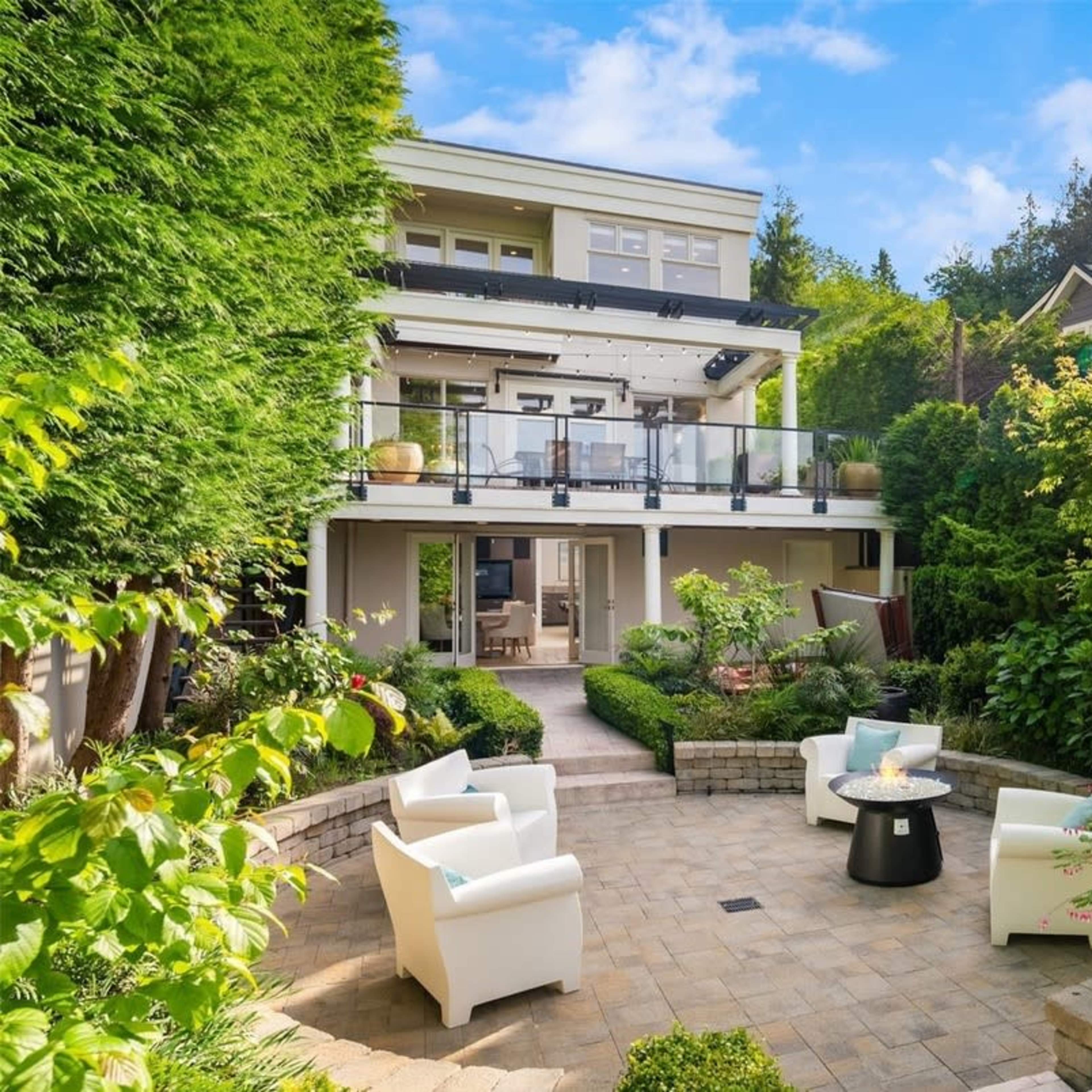 A multi-level house with a patio surrounded by lush greenery and modern outdoor furniture.
