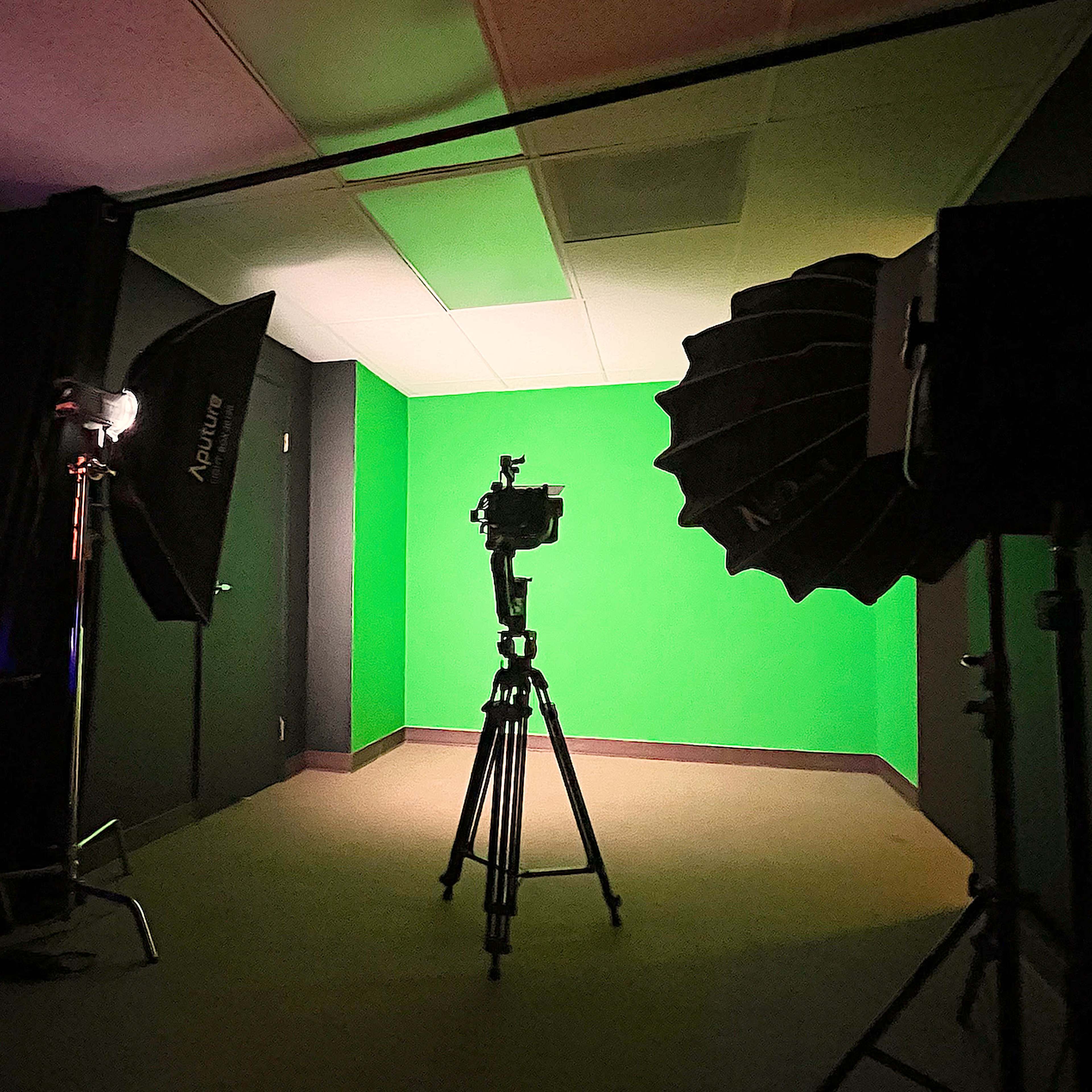 A photography studio equipped with a green screen backdrop, lighting equipment, and a camera on a tripod.