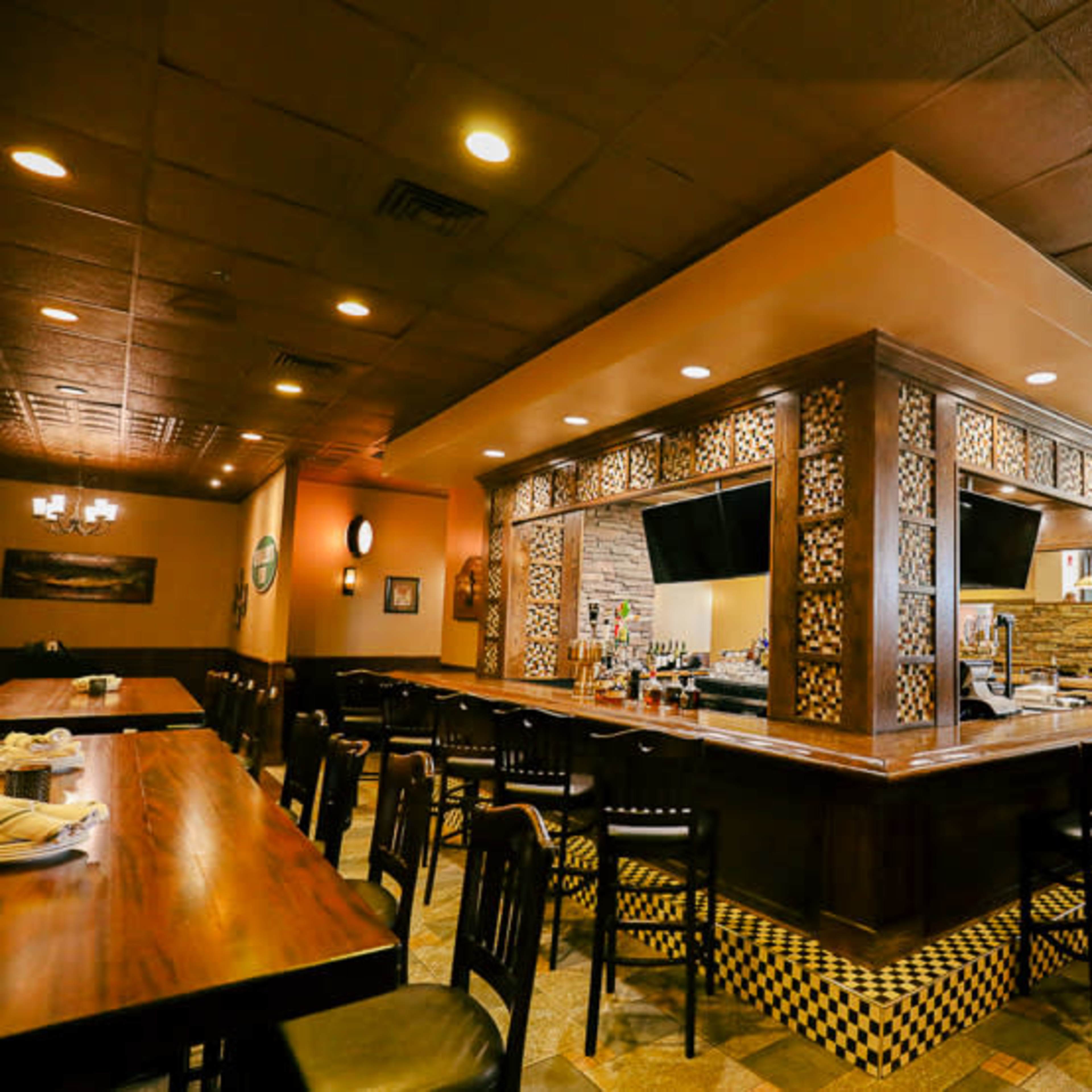 The interior of a restaurant featuring a centrally located bar with decorative woodwork and surrounding seating areas.