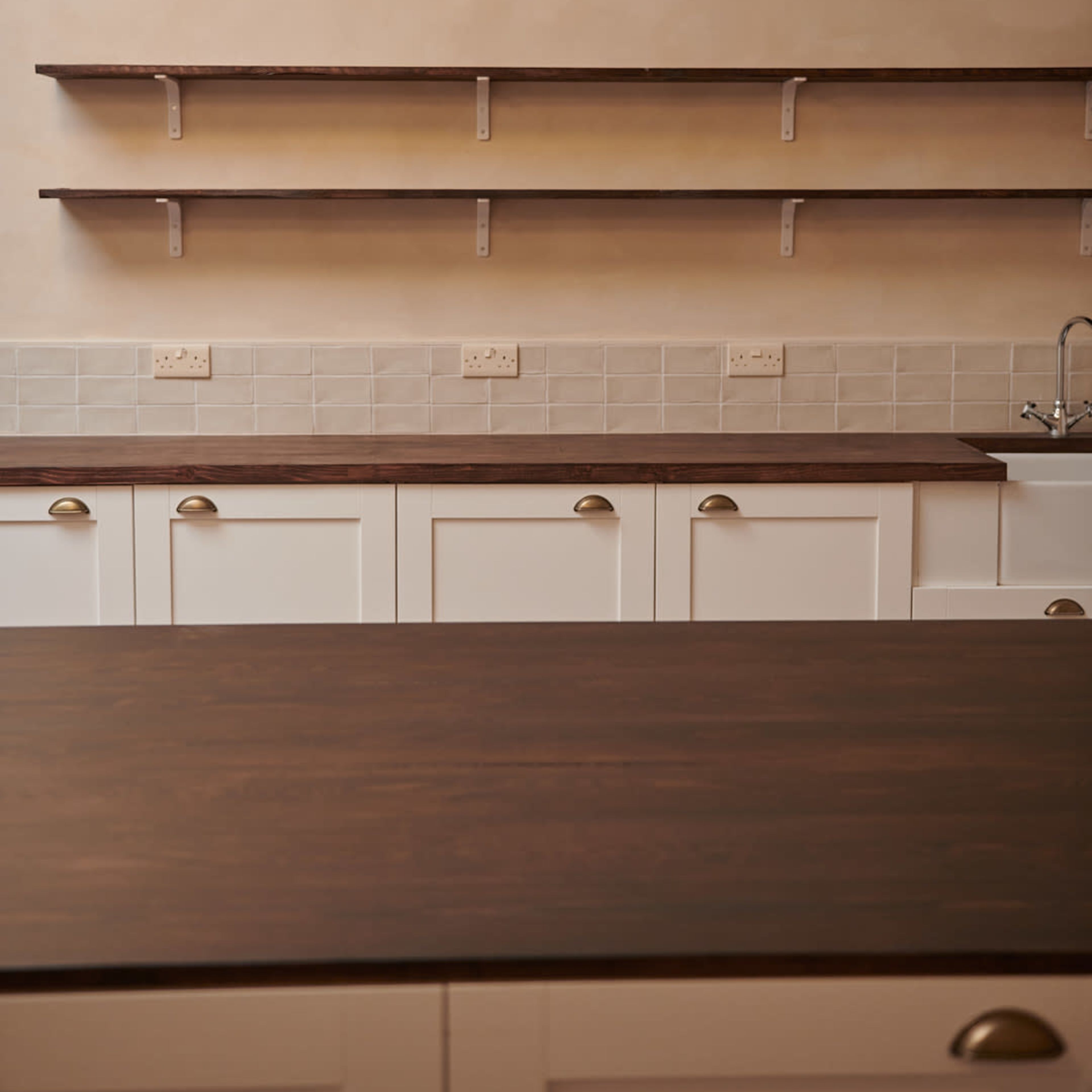 A kitchen with wooden countertops, white cabinets, and shelves against a light-colored wall.