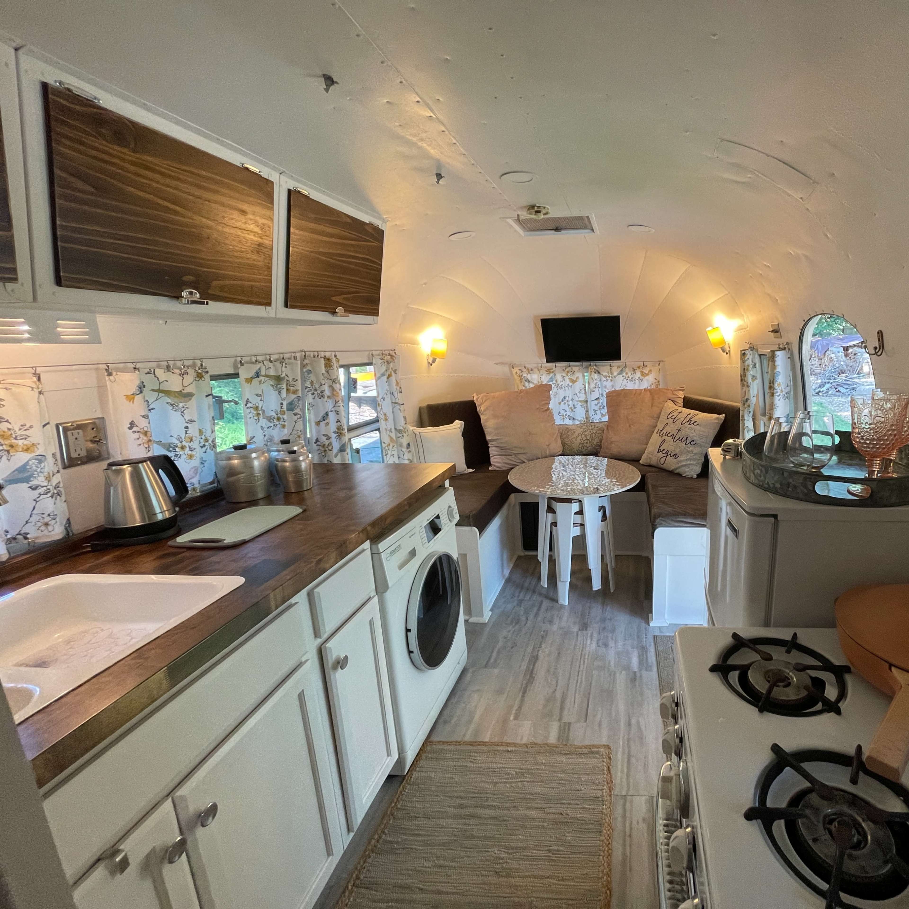 The interior of a converted vintage trailer with a kitchenette, a cozy seating area, and decorative elements.
