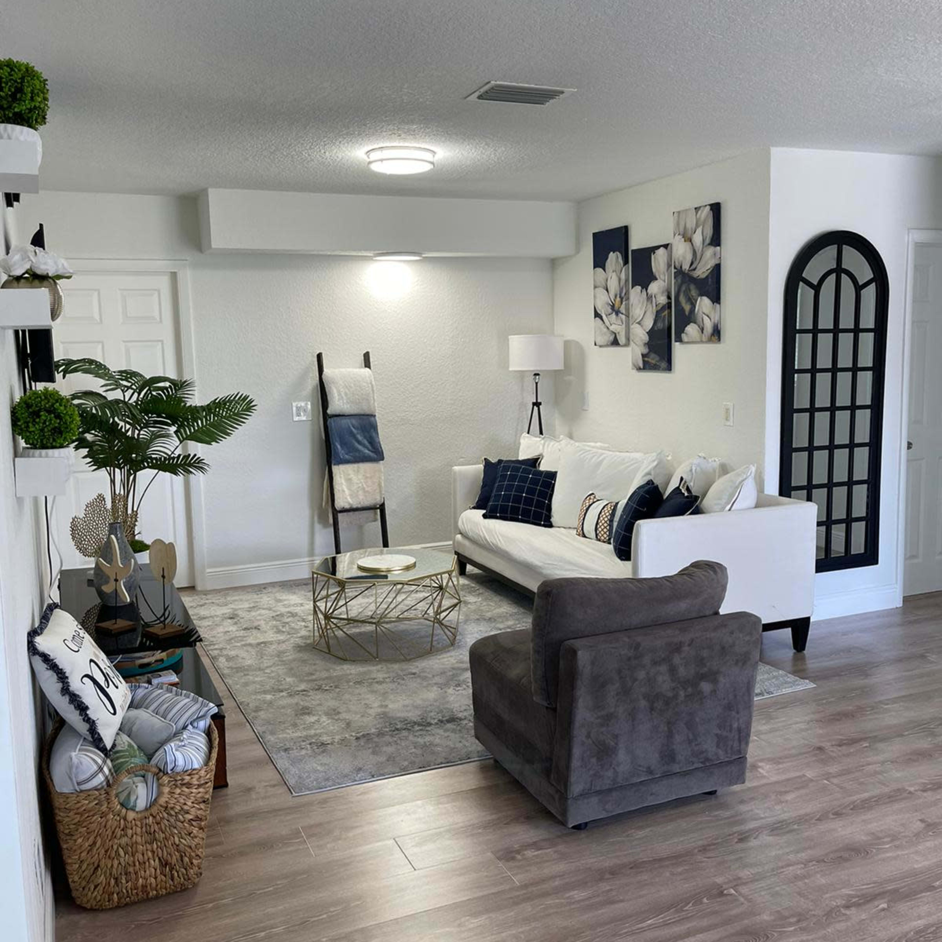 A bright living room featuring a white sofa, a gray armchair, a round coffee table, and decorative wall art with floral designs.