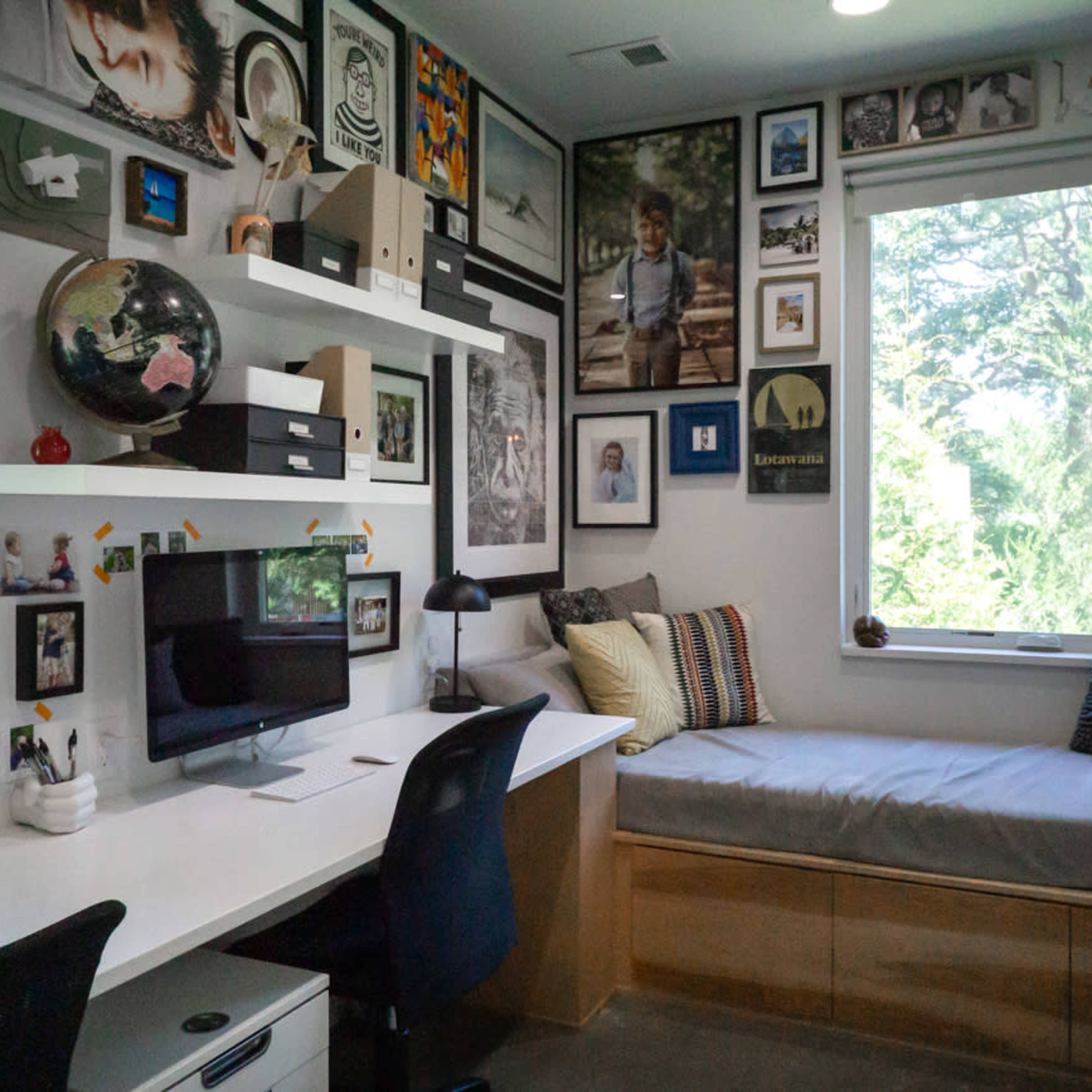 A well-organized room with a desk, computer, and a cozy seating area adorned with framed photos and decorative items on the walls.