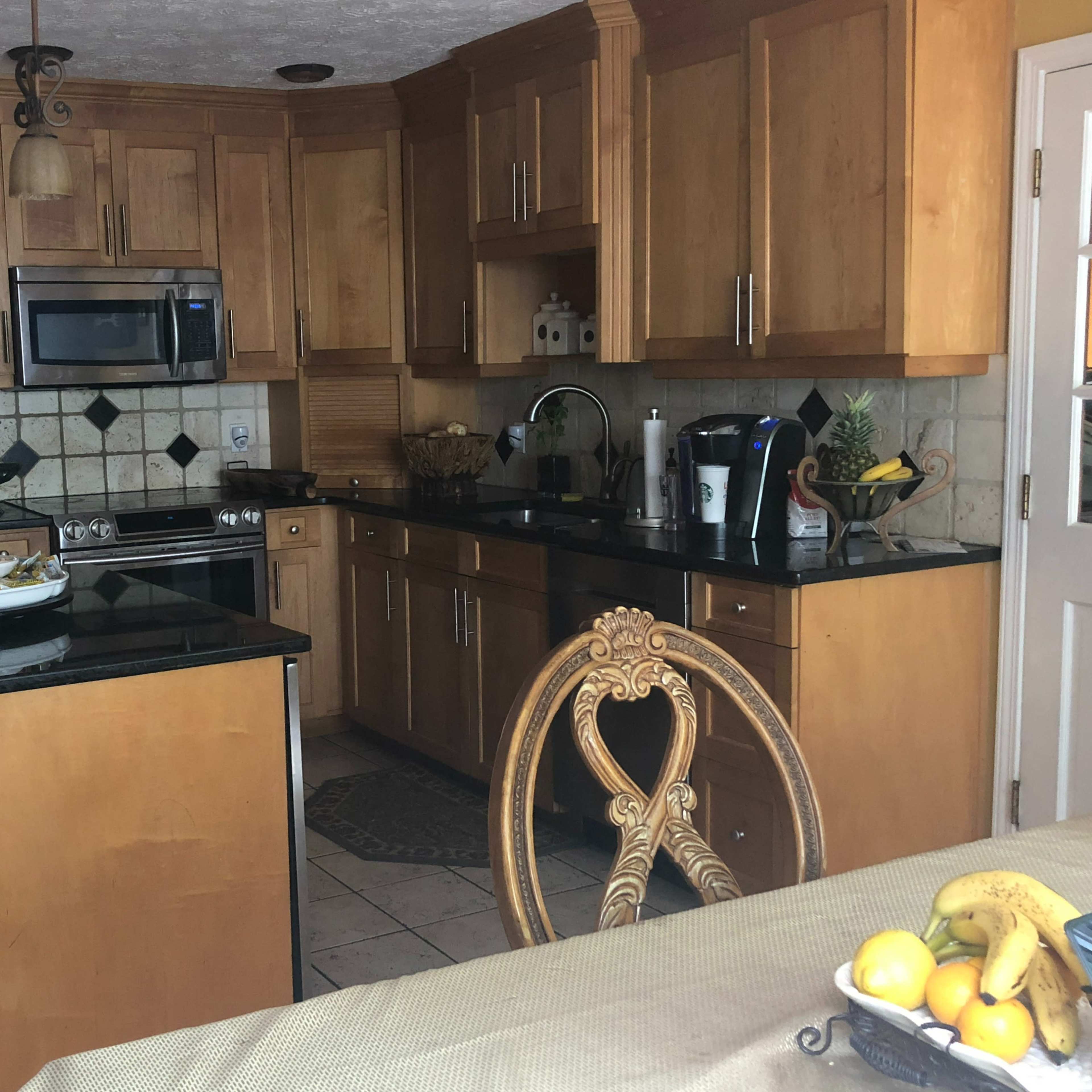 A kitchen with wooden cabinetry, black countertops, and stainless steel appliances, featuring an island with seating and a dining area.