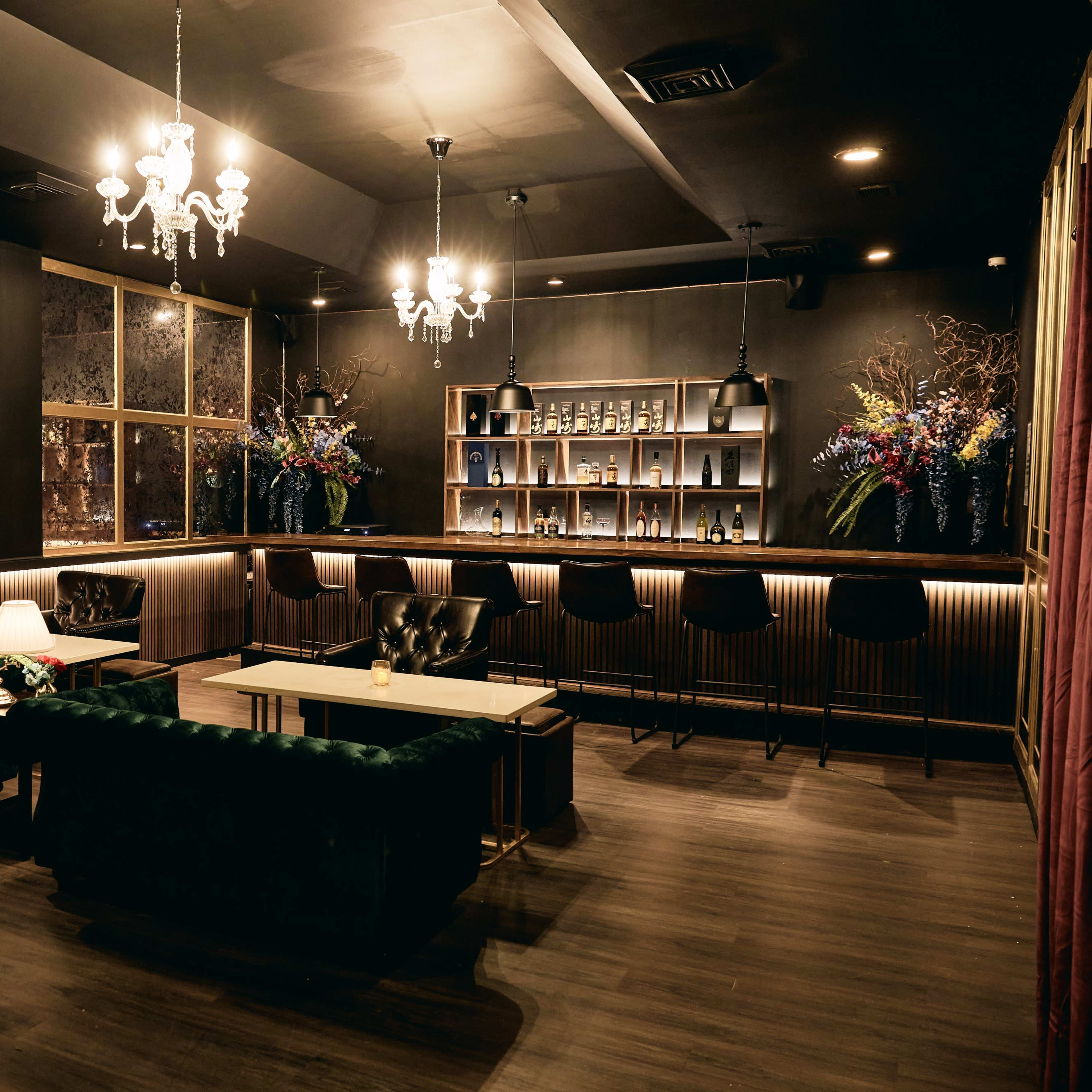 A cozy lounge with dark walls, stylish seating, shelves of books, and a well-lit bar area.