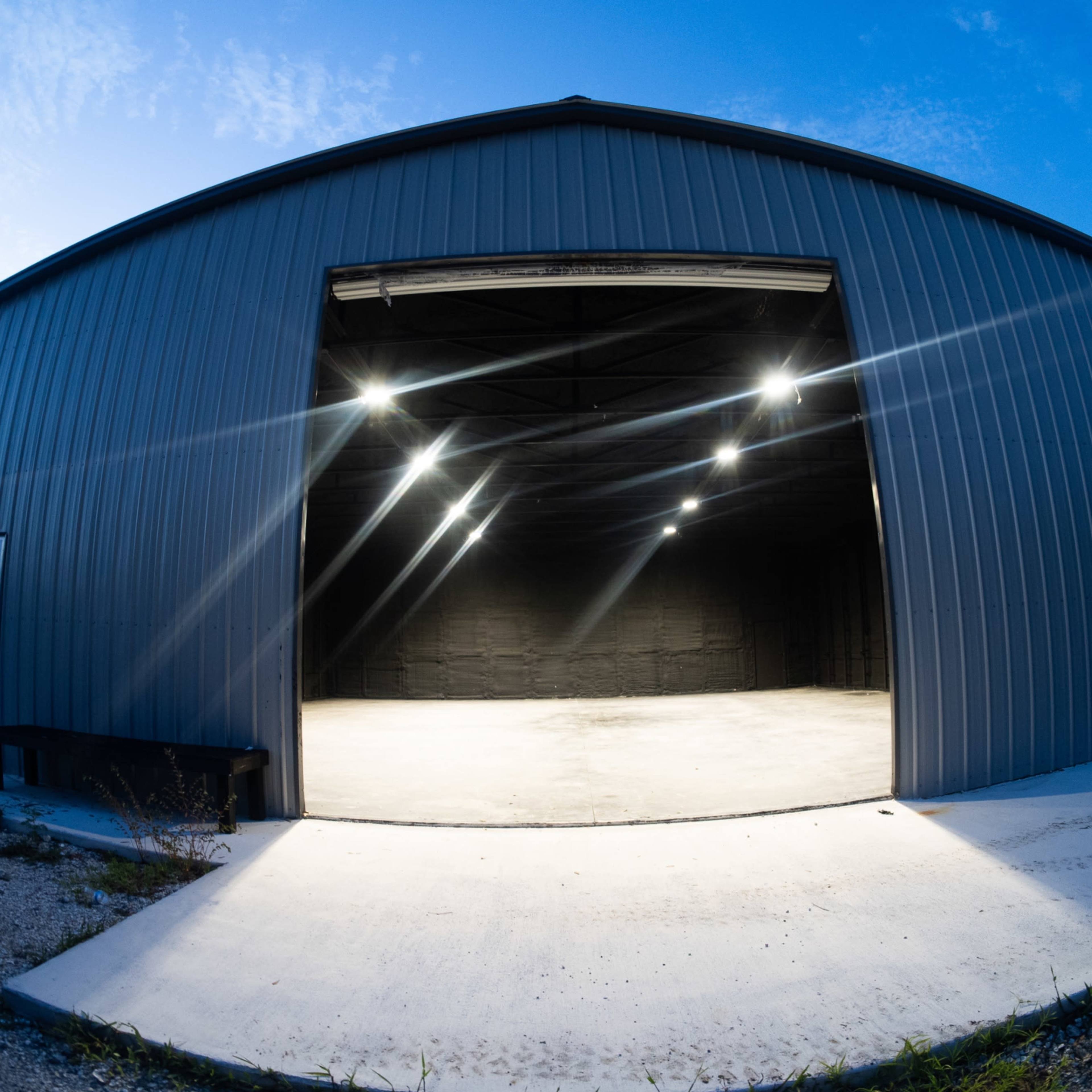 A large metal building with an open entrance, illuminated by overhead lights, and a concrete surface outside.