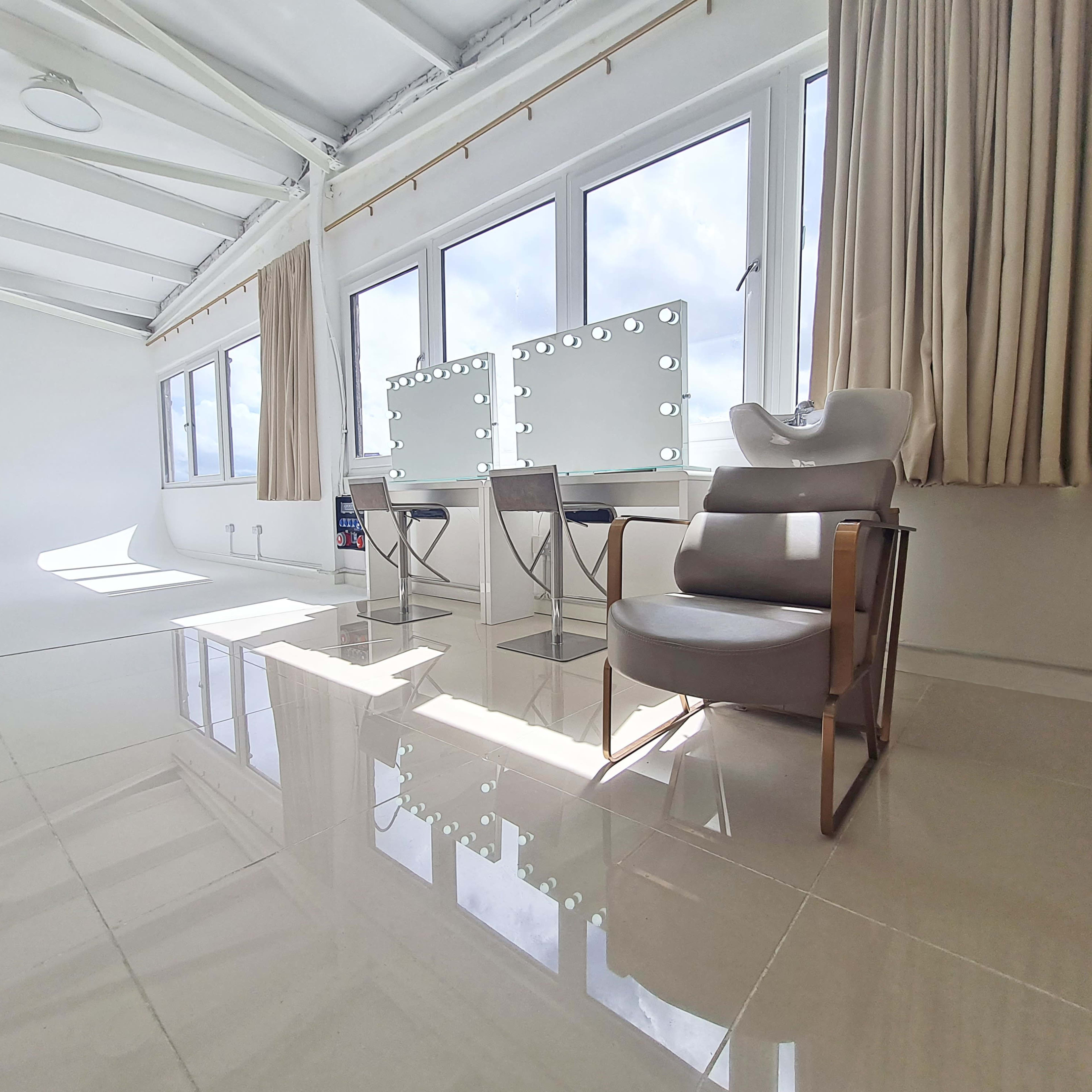 A bright, modern interior with large windows, two vanity mirrors, and a stylish chair.